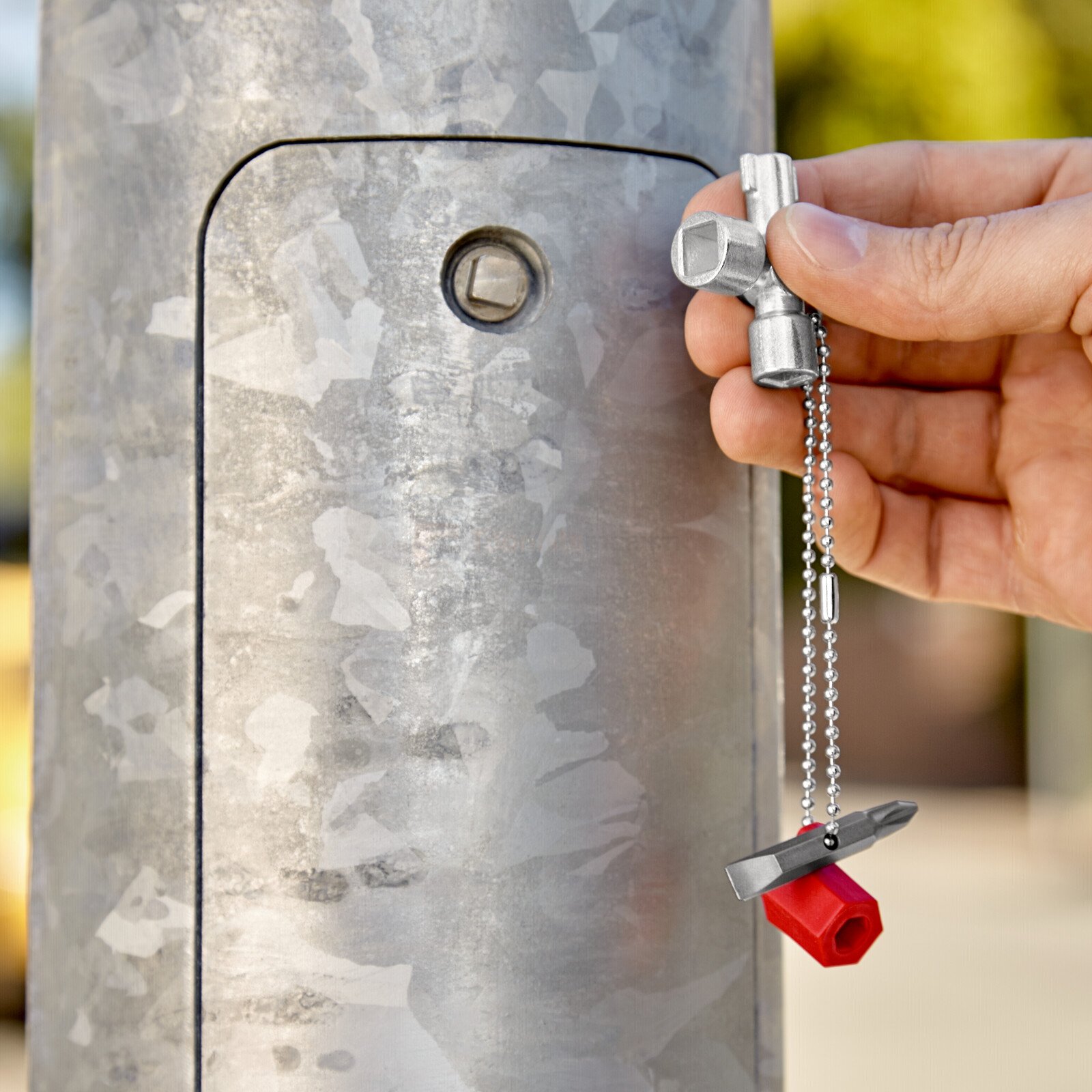 Pildil on käsi, mis hoiab KNIPEX standardvõtit hoonete tehniliste seadmete jaoks, millega avatakse metallist posti uks.