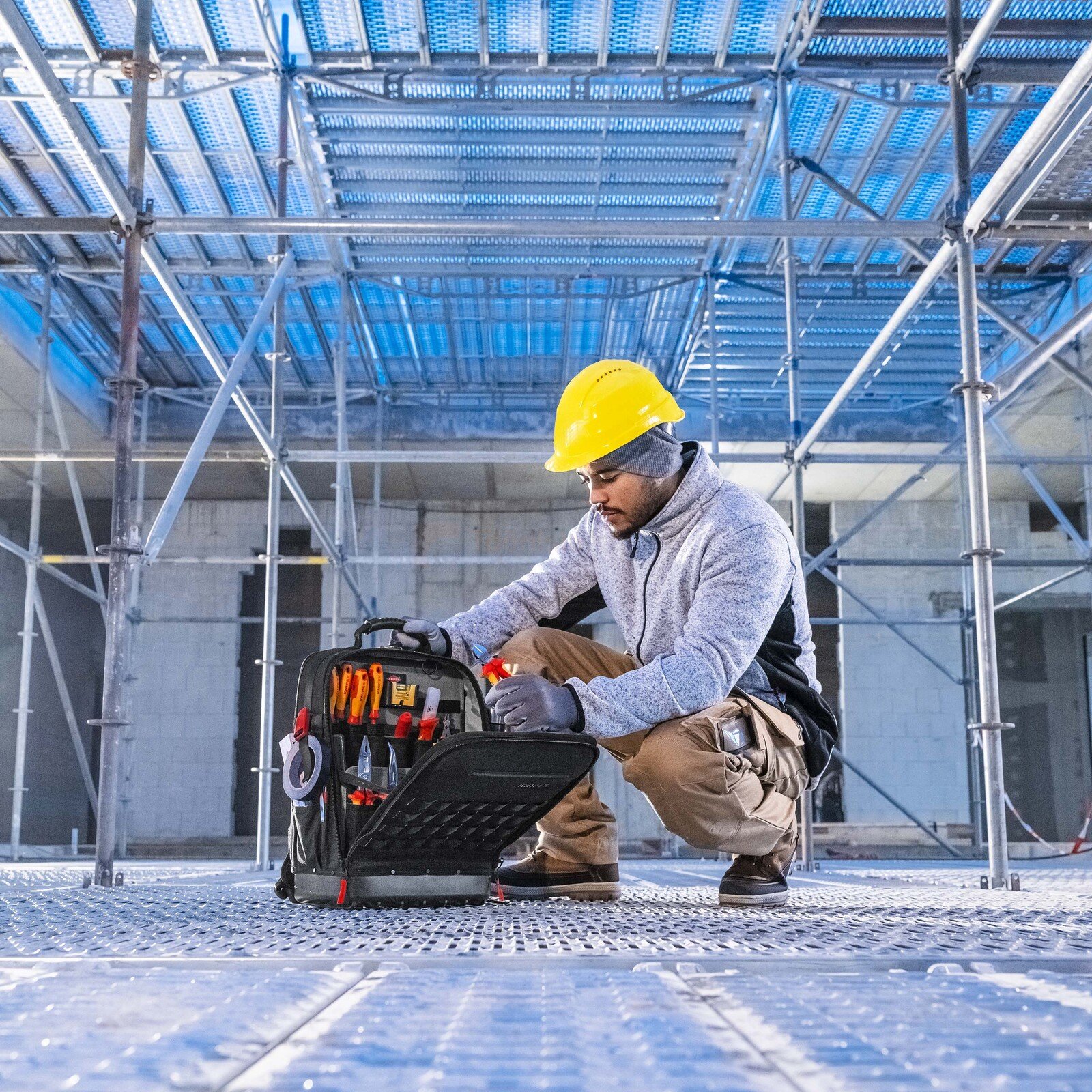 Pildil on ehitustöötaja, kes on kummargil Knipex Modular X18 tühja tööriistakasti juures, mis on avatud ja täis...