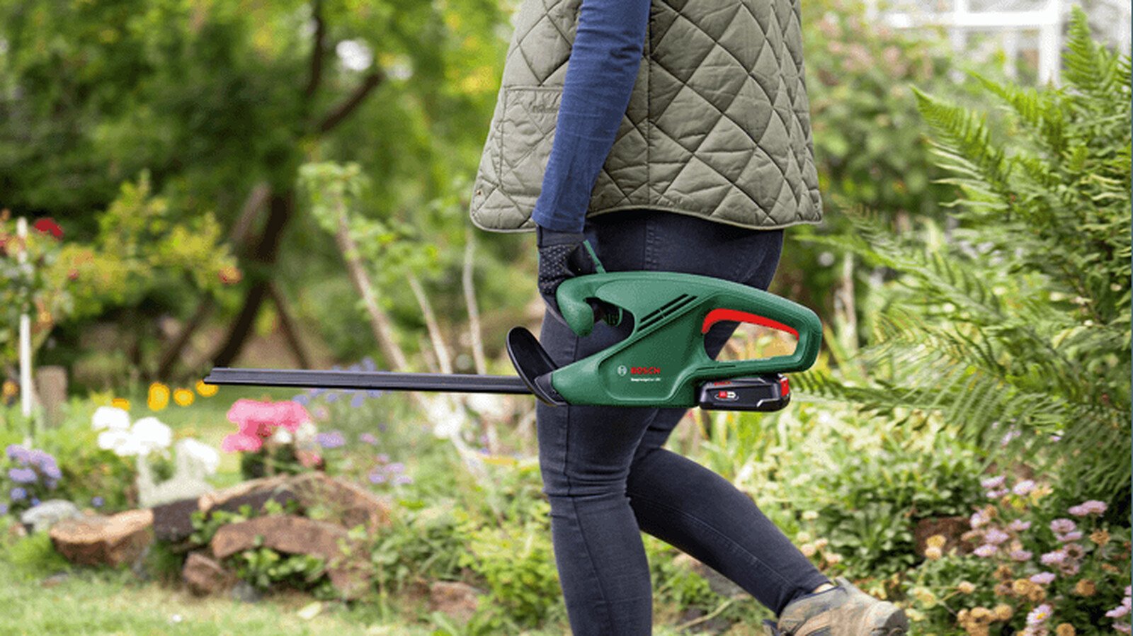 Pildil on aias jalutav inimene, kes hoiab käes Bosch akutoitega hekilõikurit EasyHedgeCut 18V-44-11.
