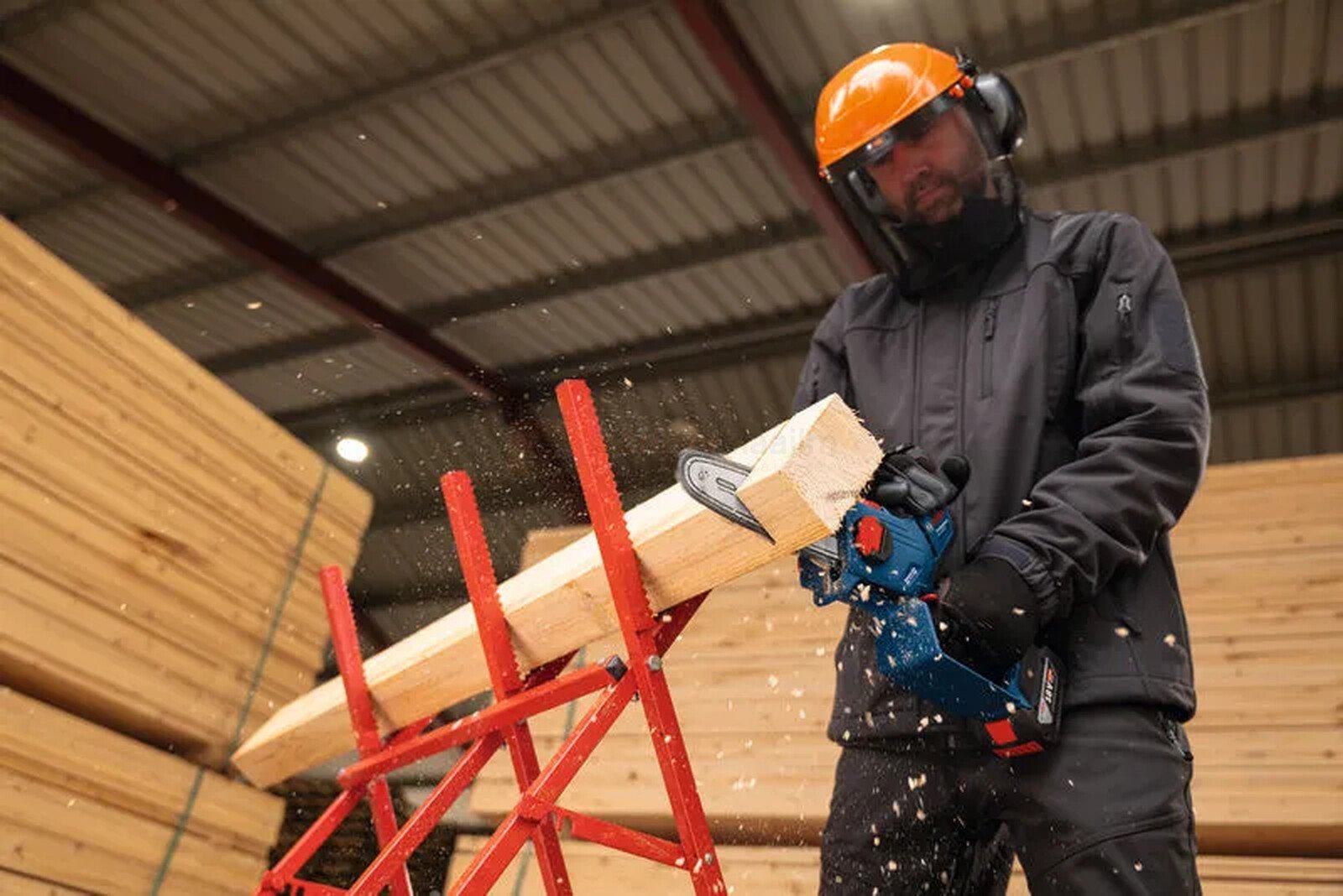 Pildil on mees, kes kasutab Bosch akukettsaagi GKE 18V-20, saagides puidutükki saeraamil, kandes samal ajal kaitsevarustust.