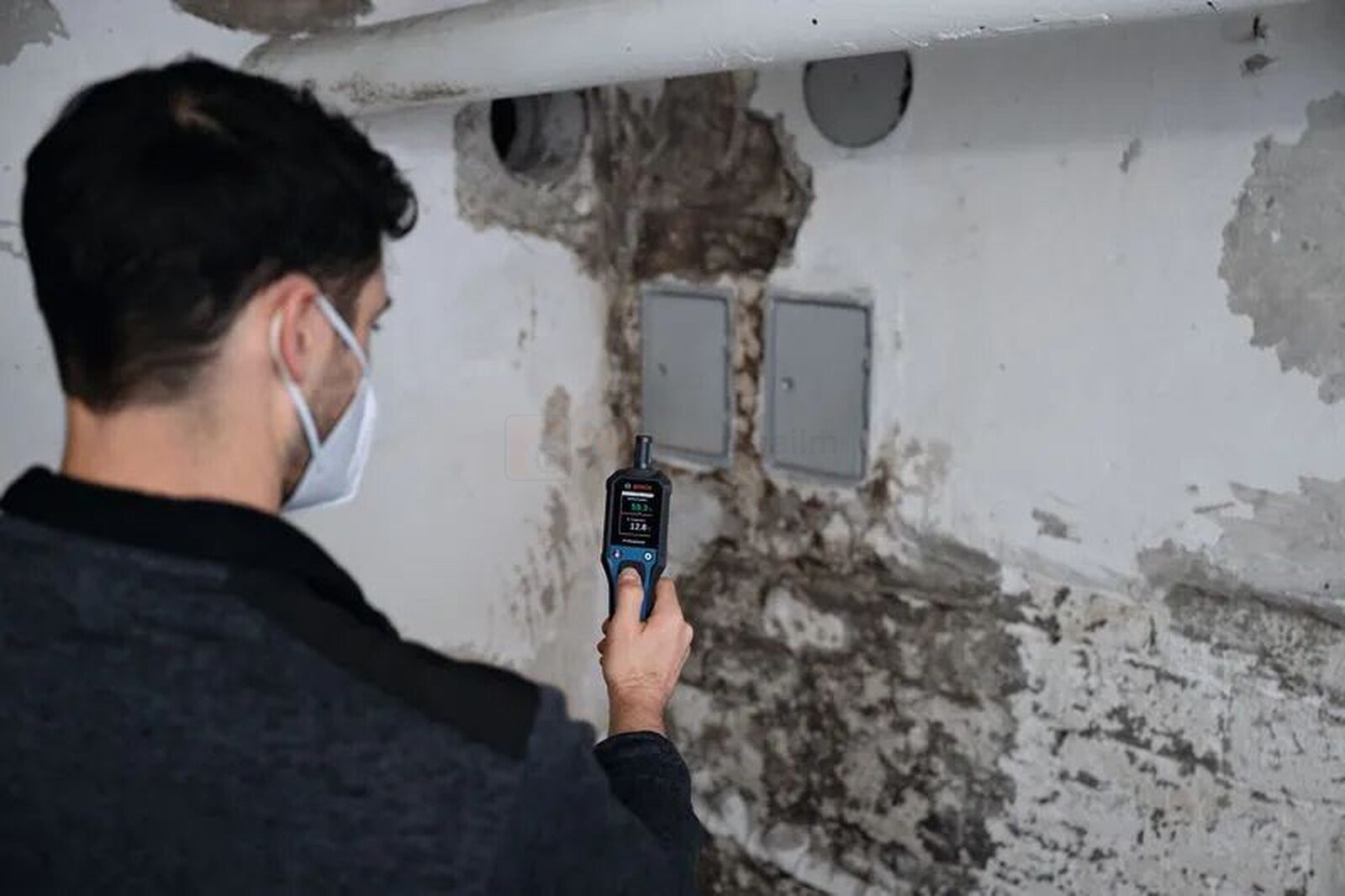 Pildil on mees, kes kasutab Bosch termo-hügromeetrit GDH 1-17 niiskuskahjustuste hindamiseks seinal.
