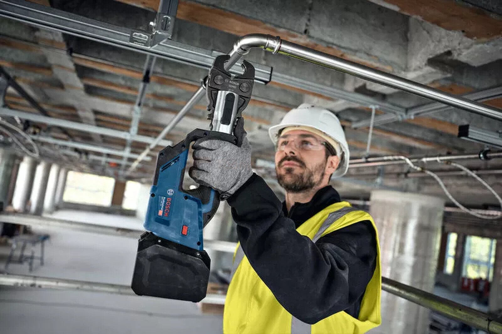 Pildil on ehitustöölise käes Bosch akutoitel torupress, mis on suunatud torude pressimisele.