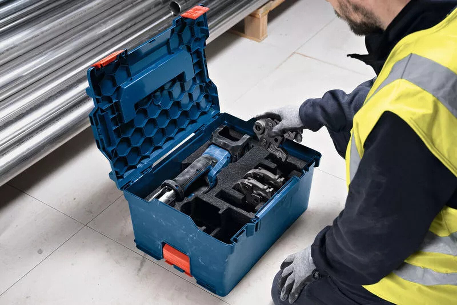 Pildil on mees, kes avab Bosch akutoitel torupressi GPT 18V-19 tööriistakasti, mis sisaldab presspihte.