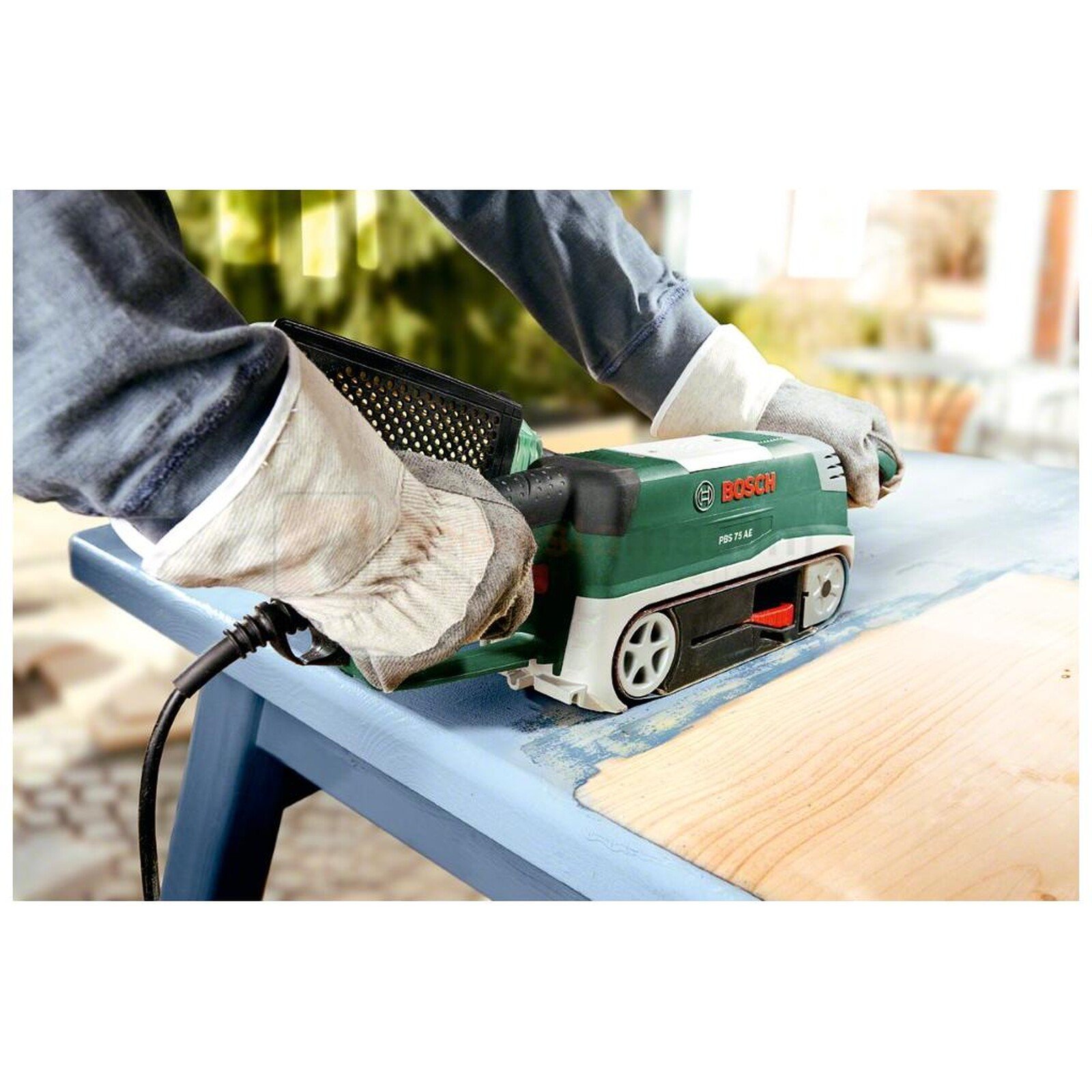 Pildil on näha, kuidas inimene kasutab Bosch lintlihvija PBS 75 AE-d, et lihvida sinist lauda.