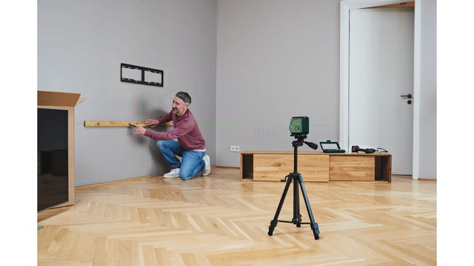 Pildil on mees, kes kasutab Bosch ristjoonlaserit AdvancedLevel 2G koos TT 120 statiiviga, et paigaldada seinale...