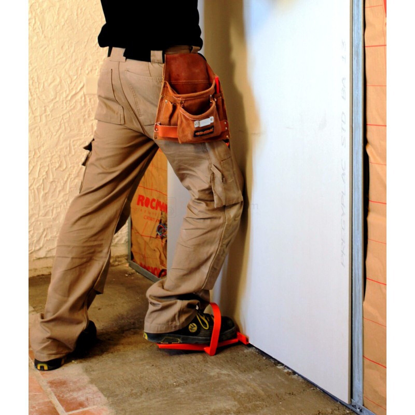 Pildil on ehitaja, kes kasutab Edma kipsplaadi positsioneerimise jalga, et hoida kipsplaati paigal.