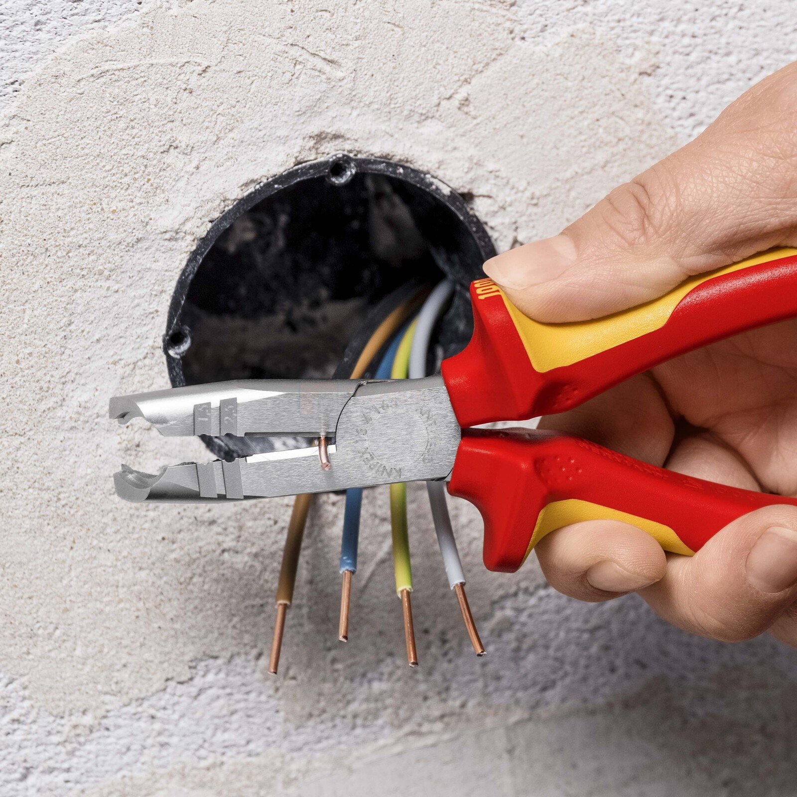 Pildil on käsi, mis kasutab Knipex koorimistange, et eemaldada elektrijuhtmete isolatsiooni.