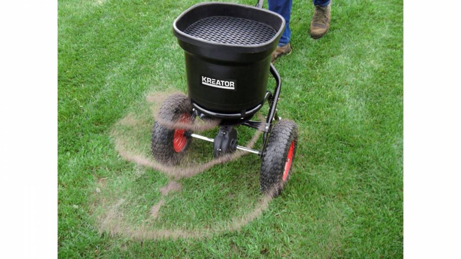 Pildil on näha, kuidas inimene kasutab murul Kreator 23 L külvikut/laoturit, mis puistab materjali.