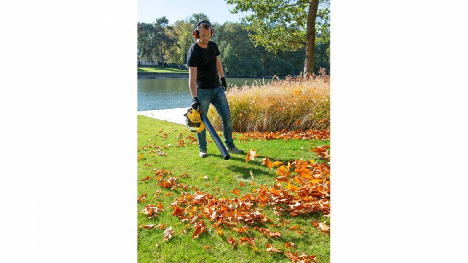 Pildil on näha inimene, kes kasutab Powerplus X lehepuhurit POWXG50400, et puhuda lehti murult.