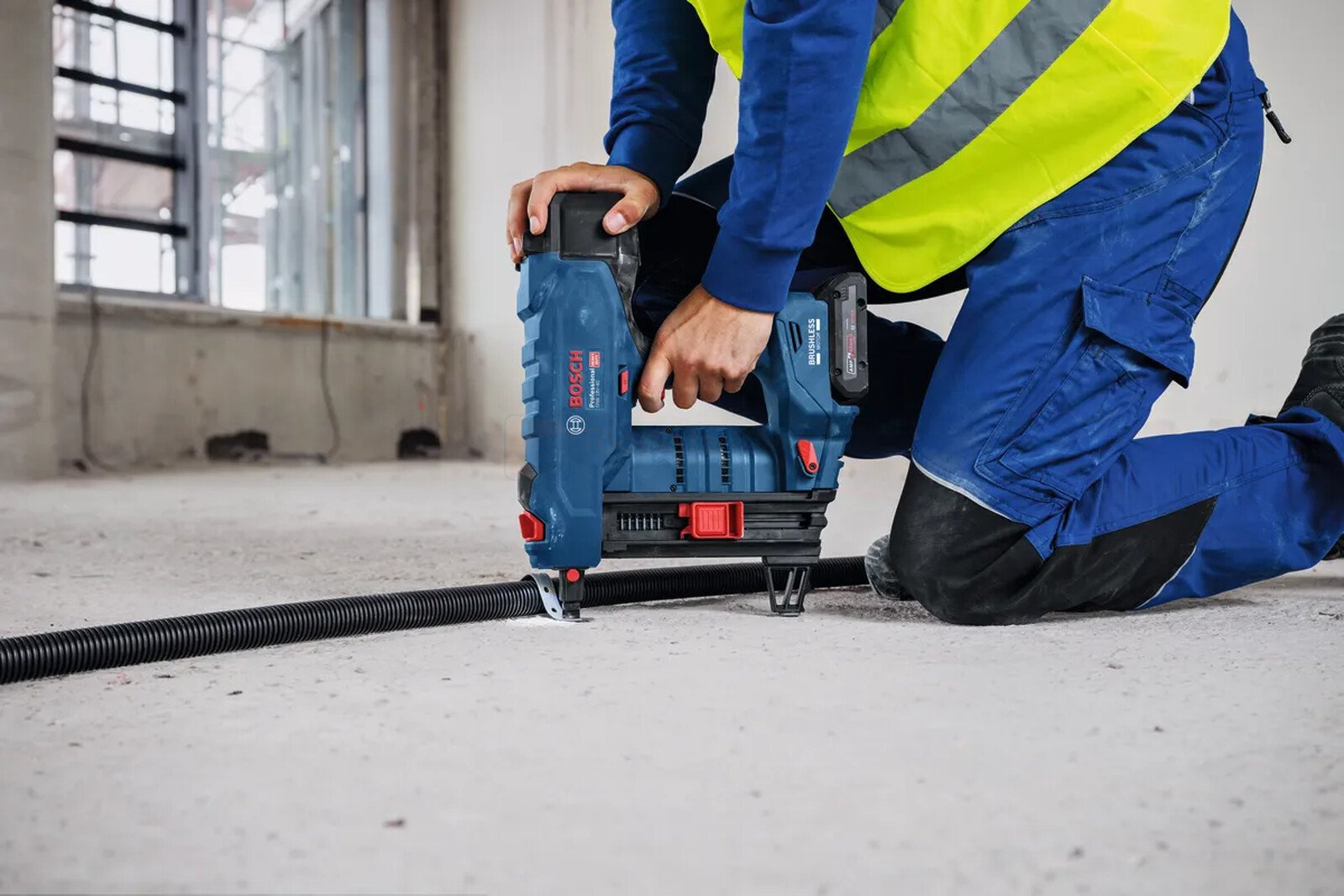 Pildil on ehitaja, kes kasutab Bosch'i kinnitusseadet, et kinnitada musta toru põrandale.