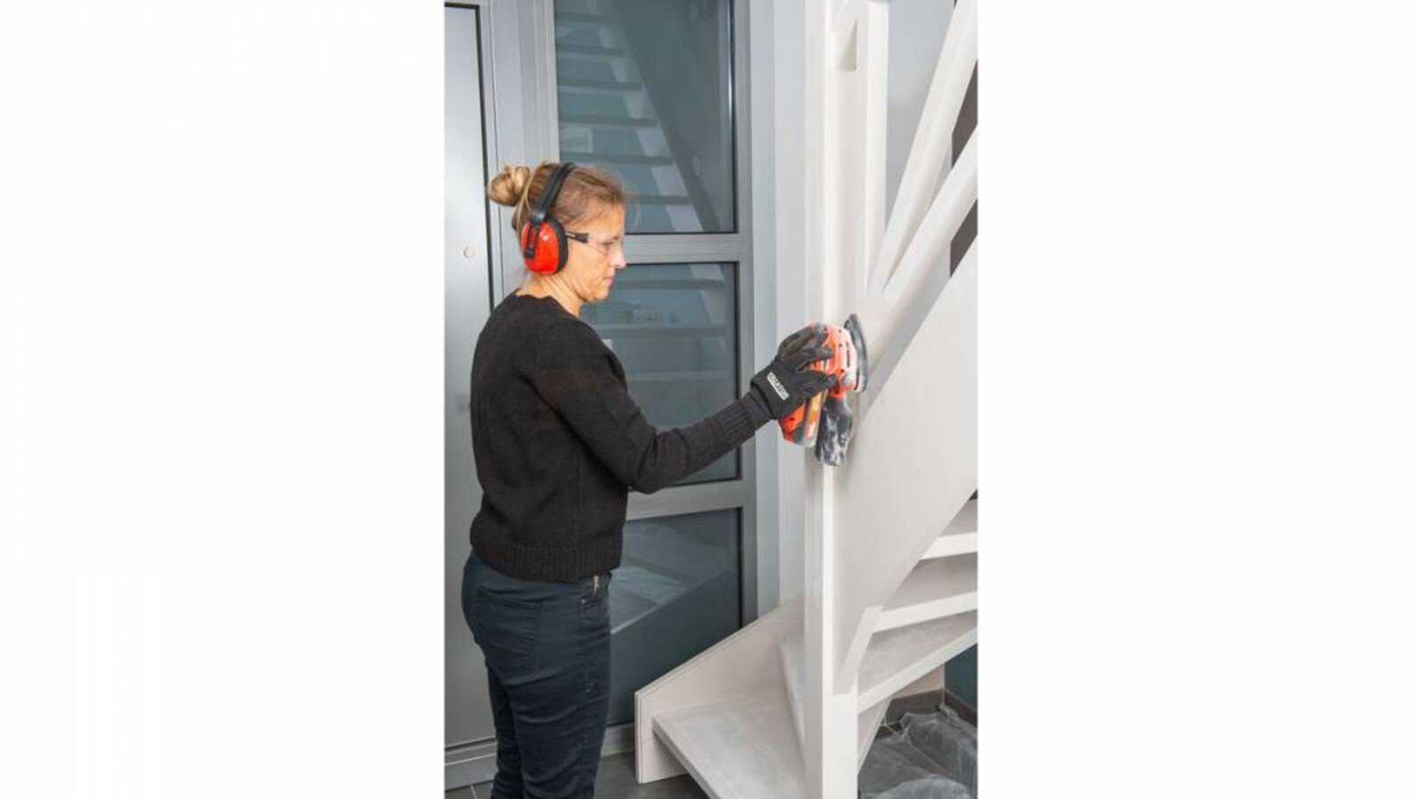 Pildil on naine, kes lihvib treppi akukolmnurklihvija Powerplus Dualpower abil, kandes samal ajal kõrvaklappe ja kindaid.
