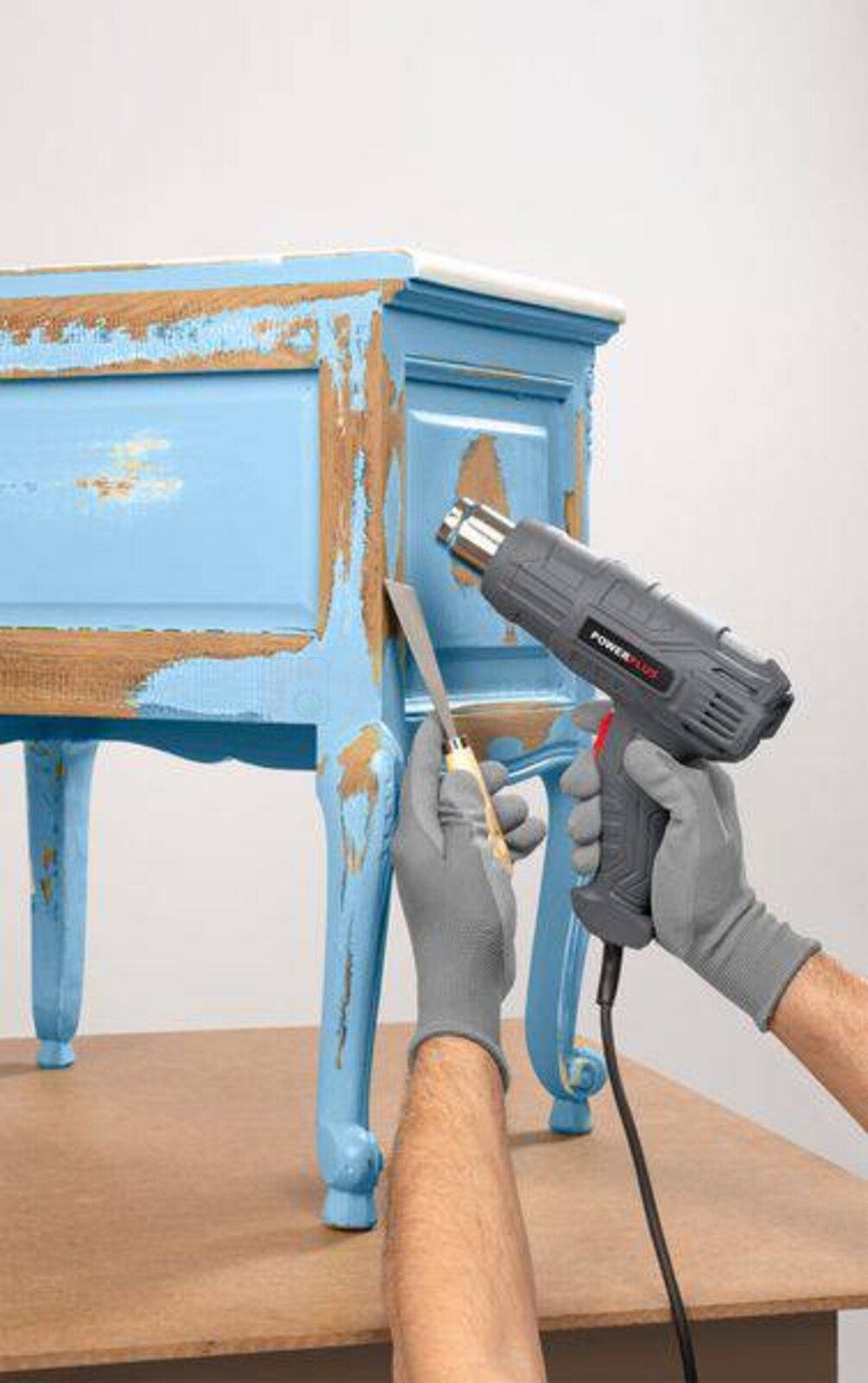 Pildil on näha, kuidas inimene kasutab Powerplus E kuumaõhupuhurit POWE80041 mööblilt vana värvi eemaldamiseks.