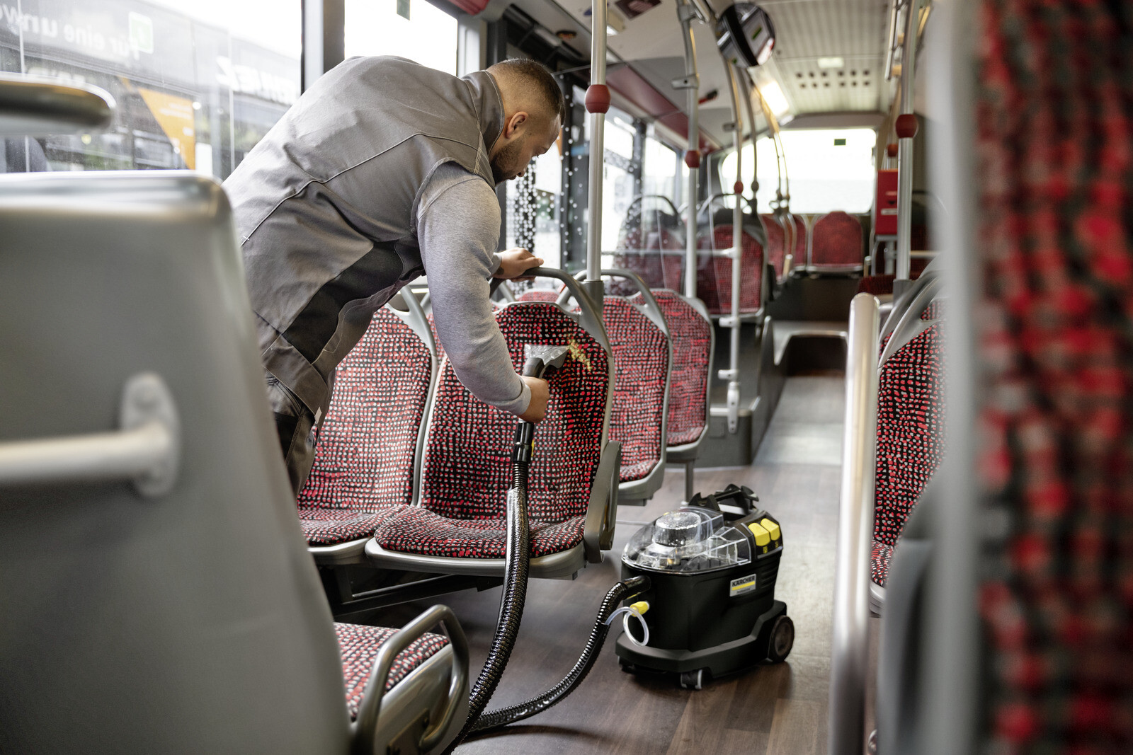 Pildil on näha meest, kes kasutab Kärcher Puzzi 8/1 Go!Further tekstiilipesurit bussi istmete puhastamiseks.