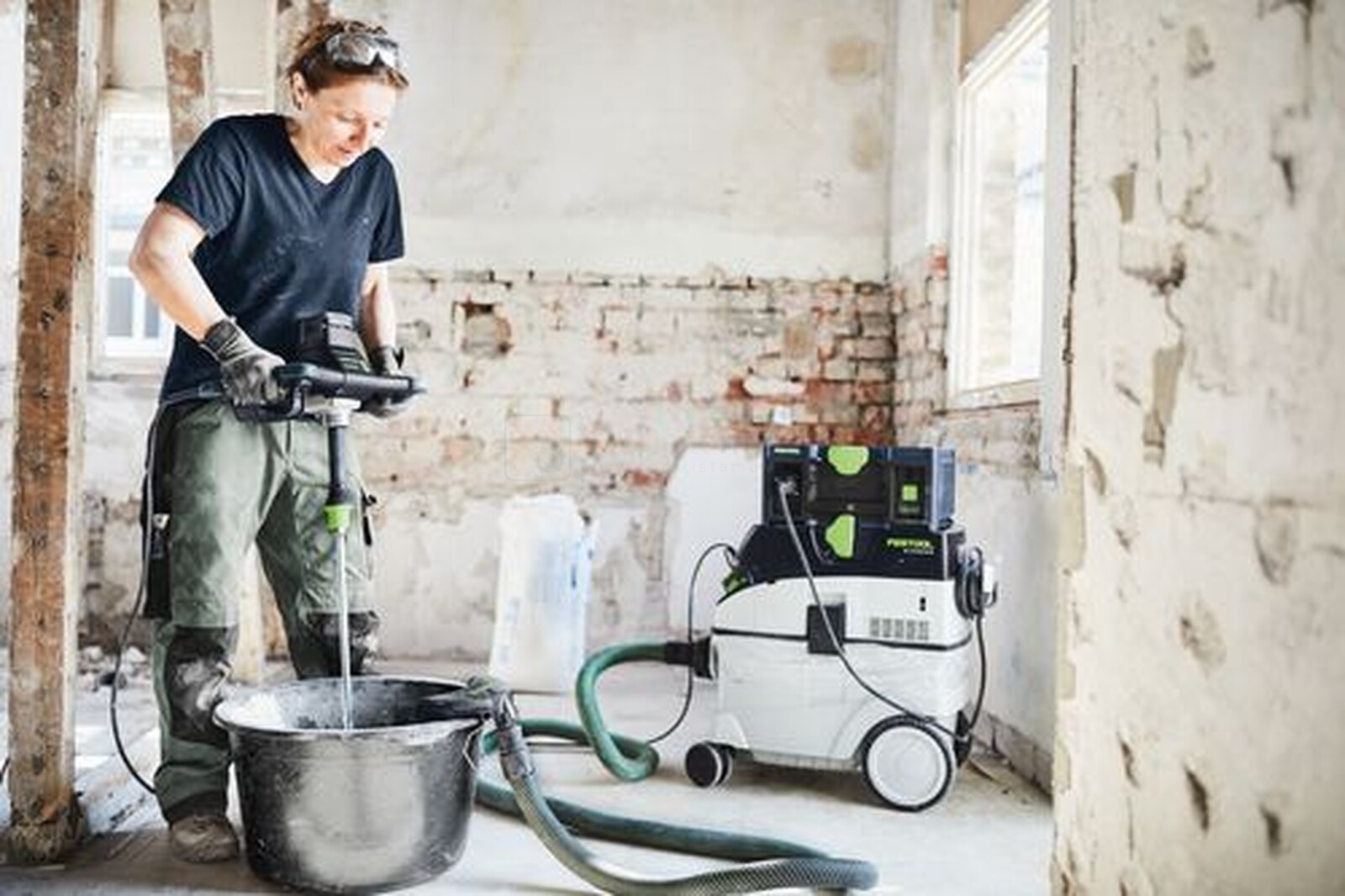 Pildil on ehitaja, kes kasutab Festool segamismasinat, samal ajal kui läheduses on Festool mobiilne akupank...