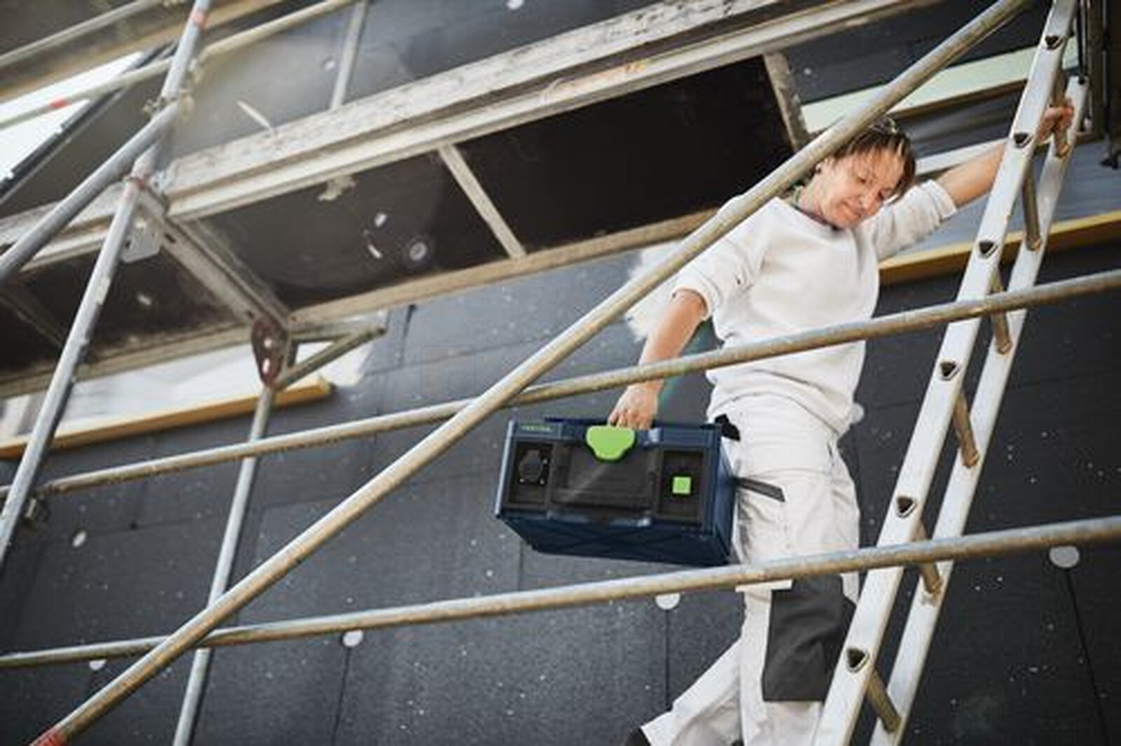 Pildil on ehitustööline, kes ronib redelil, hoides käes Festool mobiilset akupanka SYS-PowerStation SYS-PST 1500 Li HP...