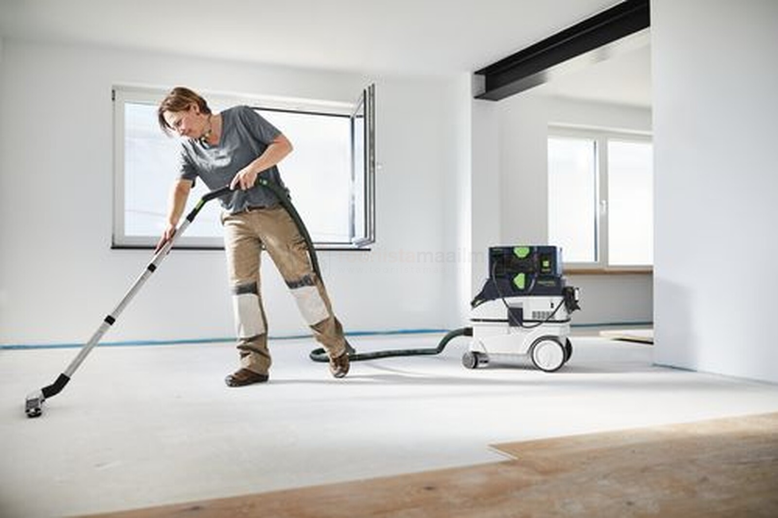 Pildil on mees, kes kasutab Festool mobiilset akupanka SYS-PowerStation SYS-PST 1500 Li HP, et tolmuimejaga põrandat...