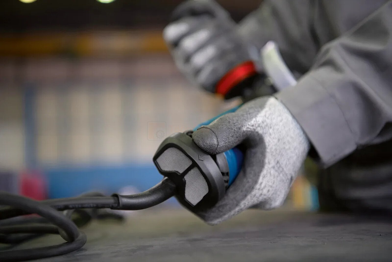 Pildil on näha, kuidas inimene hoiab käes Bosch tolmufiltriga GWS/GWX nurklihvijat, kandes samal ajal kaitsekindaid.