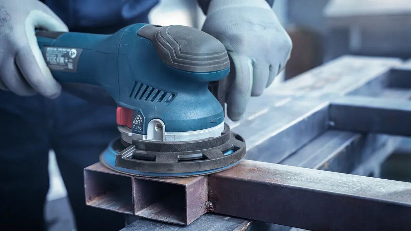 Pildil on näha, kuidas inimene kasutab Bosch fooliumlihvketast EXPERT O780 125 mm metallkonstruktsiooni lihvimiseks.