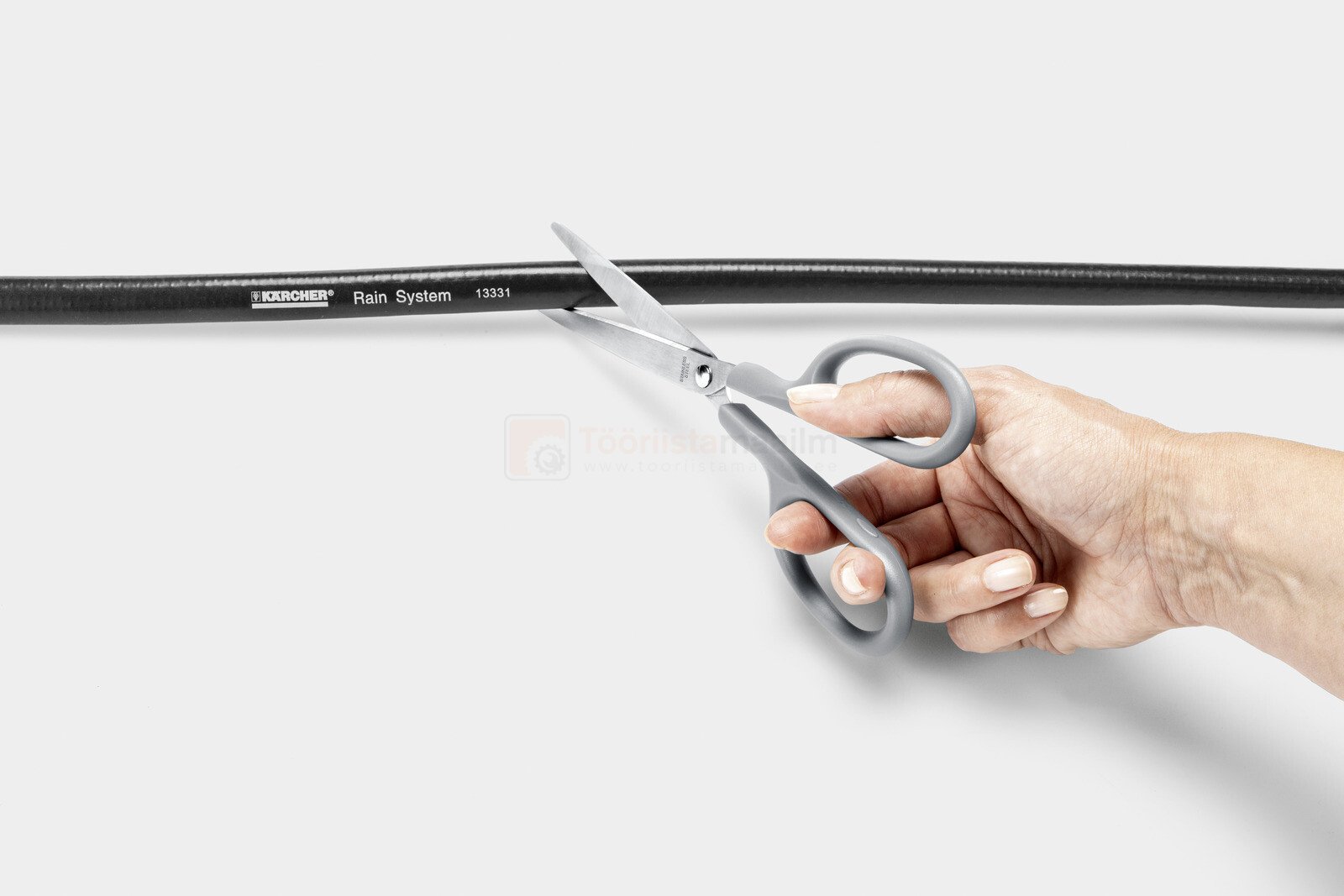 Pildil on näha, kuidas inimene lõikab Kärcheri 1/2" 10 m voolikut kääridega.