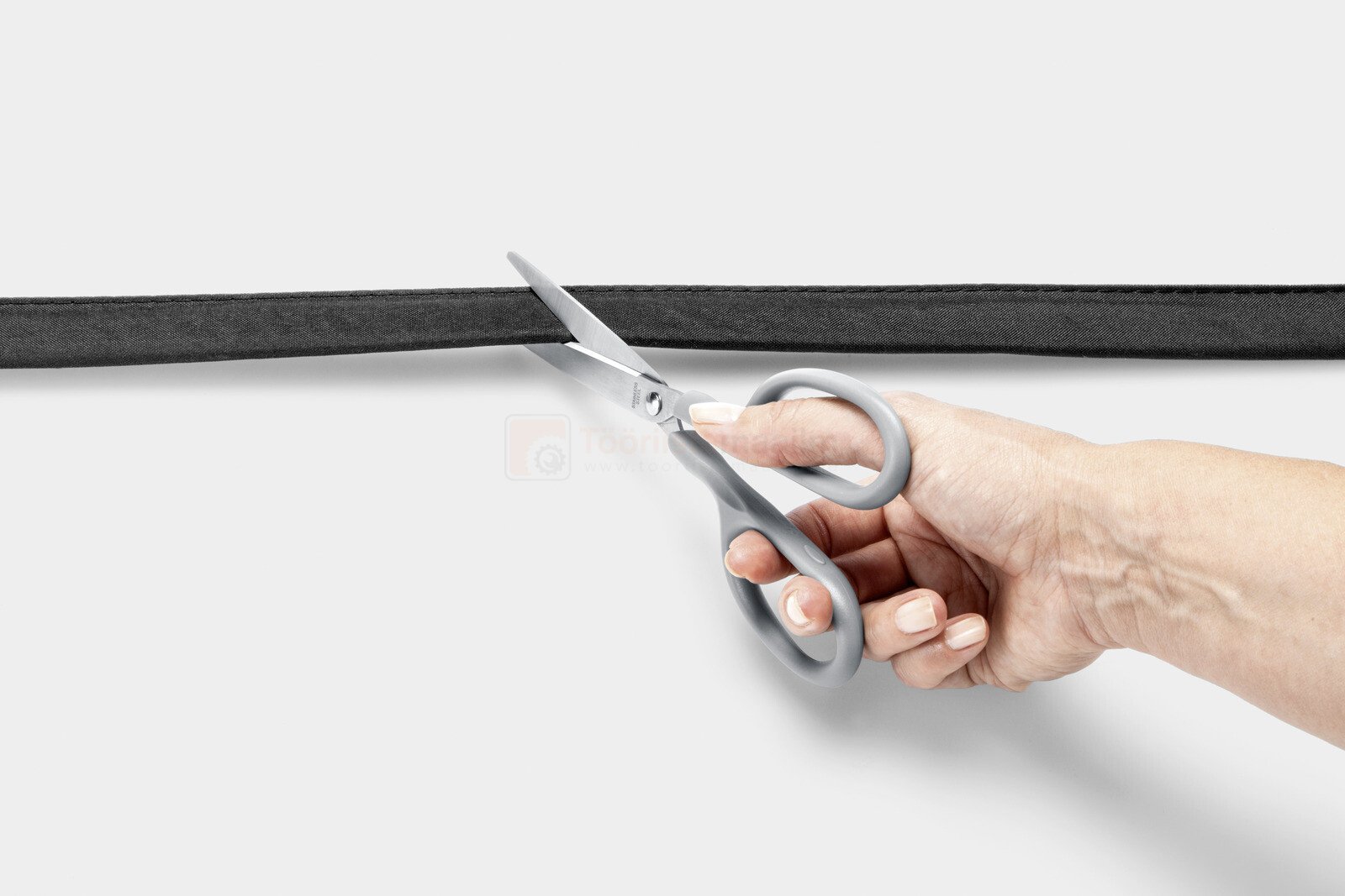 Pildil on käsi, mis lõikab kääridega Kärcheri niisutusvoolikut 1/2" 25 m.