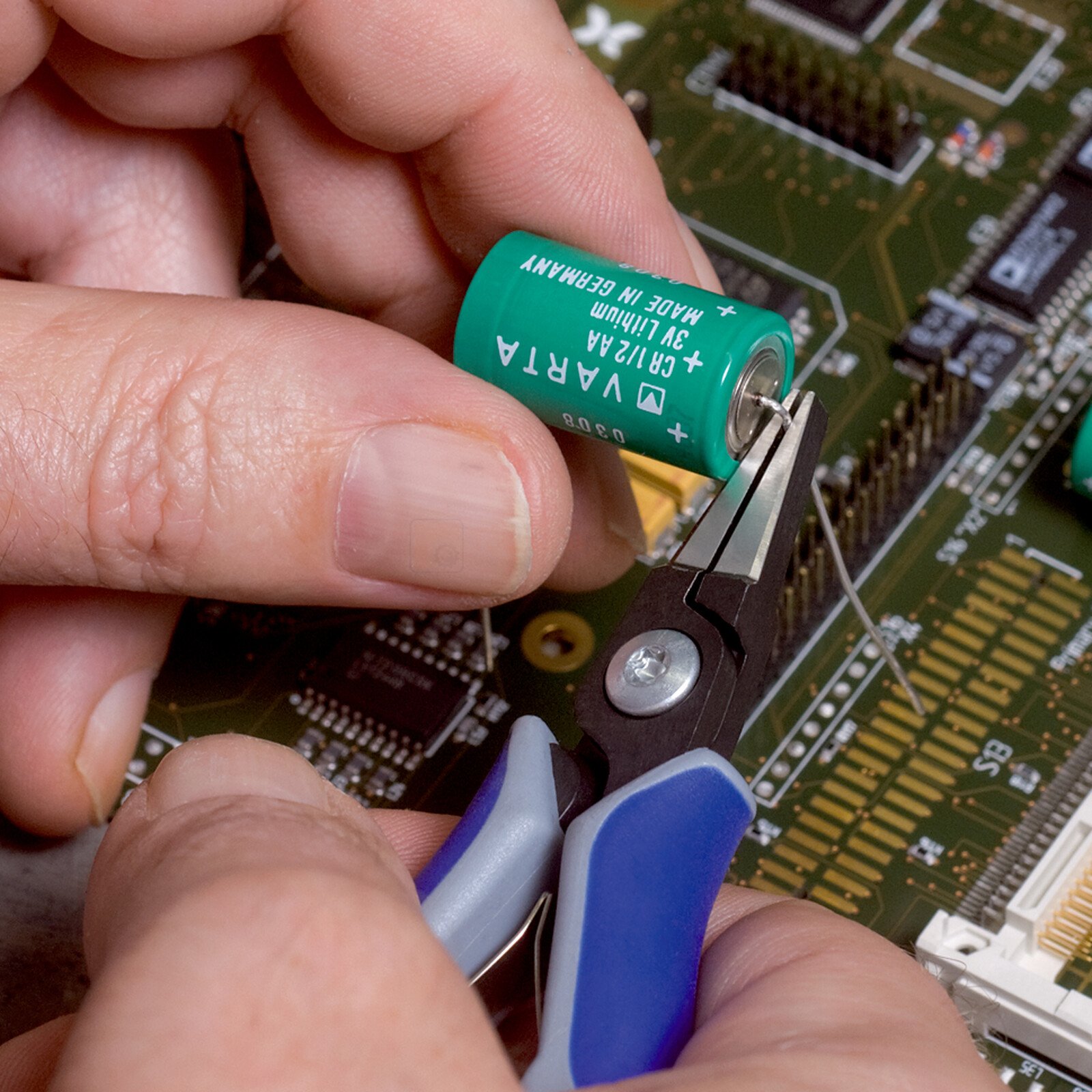 Pildil on näha, kuidas inimene kasutab Knipex täppis-elektroonika haarats-tangid, et manipuleerida väikese akuga...