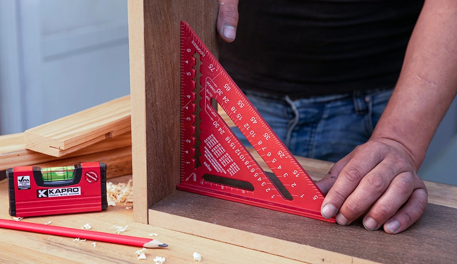 Pildil on näha, kuidas inimene kasutab Kapro 300 mm puusepa nurgikut puidutöö tegemisel, samal ajal kui laual on ka teisi...