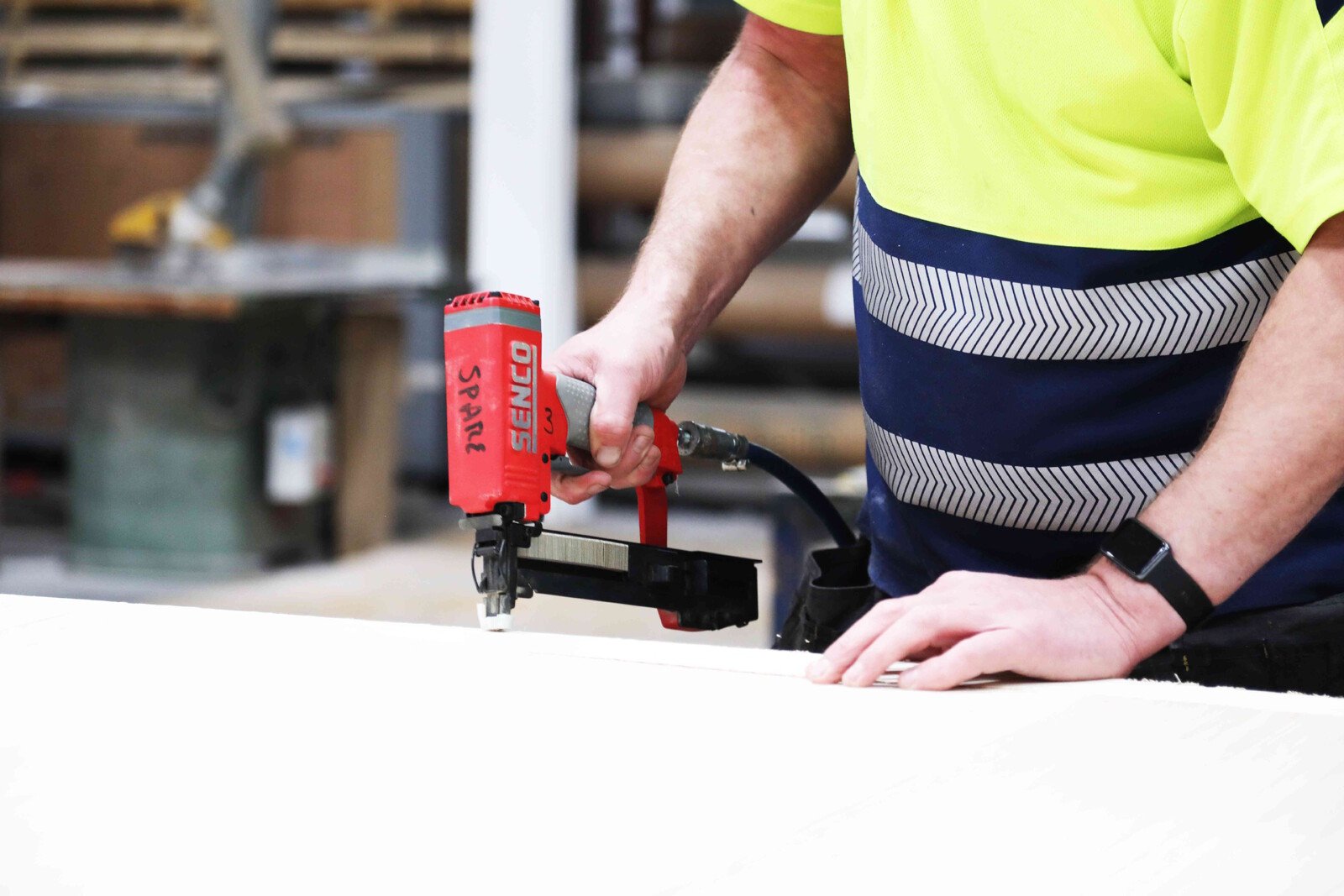 Pildil on mees, kes kasutab SENCO klambripüstolit SLS20MG-M, et kinnitada midagi valgele pinnale.