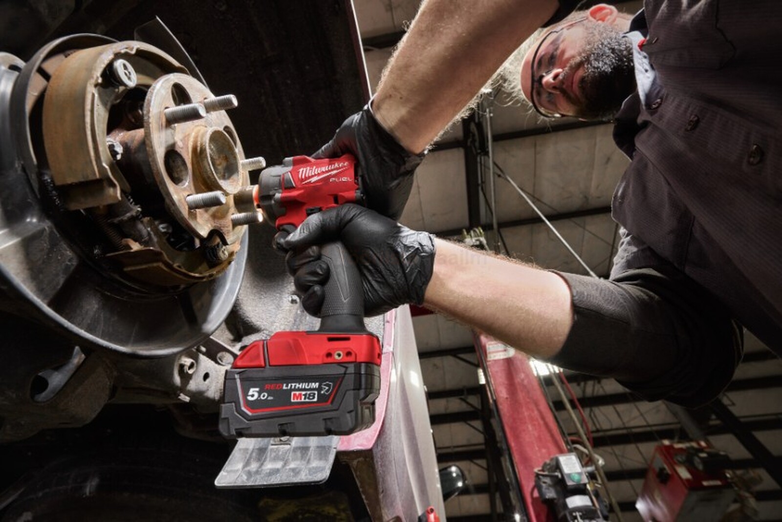 Pildil on mees, kes kasutab Milwaukee M18 B5-CR akutrelliga autol ratta kinnituspolte lahti keerates.
