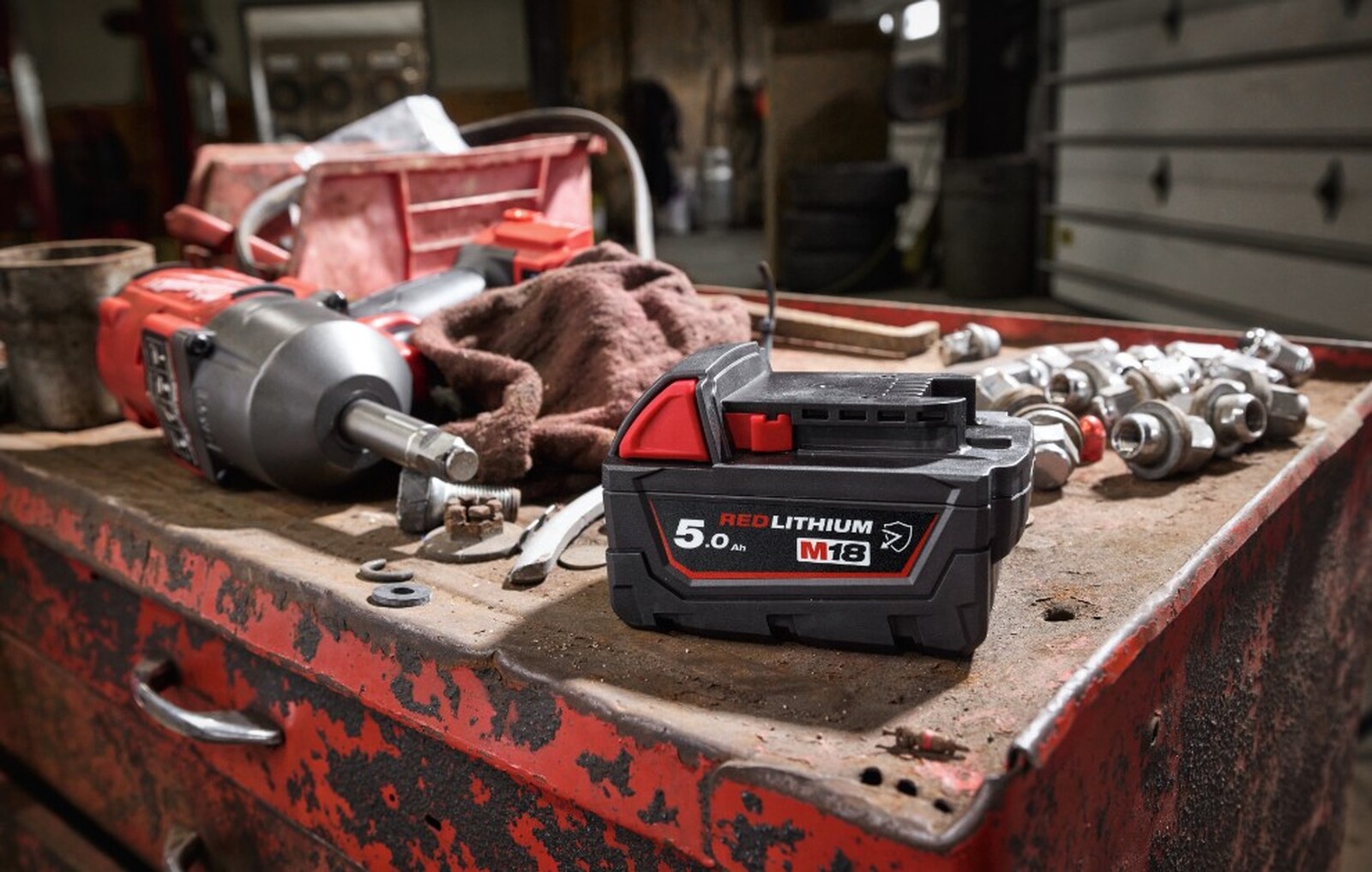 Pildil on Milwaukee M18 B5-CR - 5,0 Ah aku, mis on asetatud koos teiste tööriistadega töölauale.