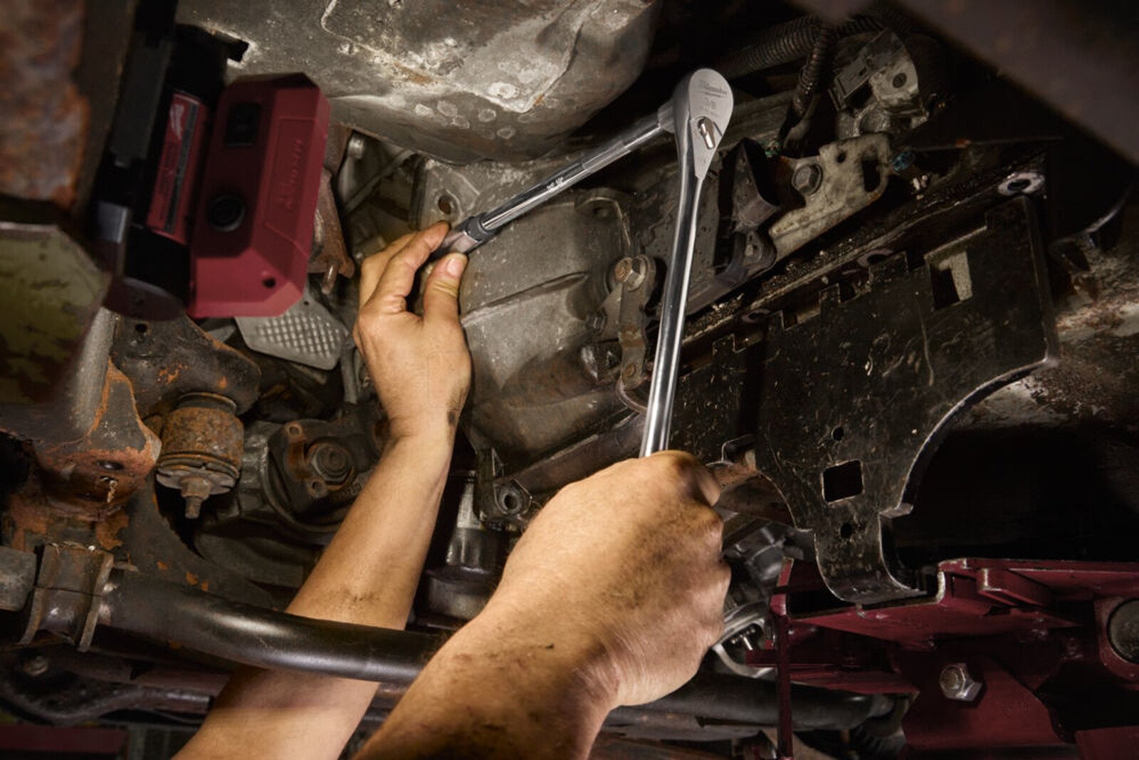 Pildil on mehaanik, kes kasutab Milwaukee pikenduste komplekti 3/8" 76-254 mm, 3-osaline, et töötada auto all.