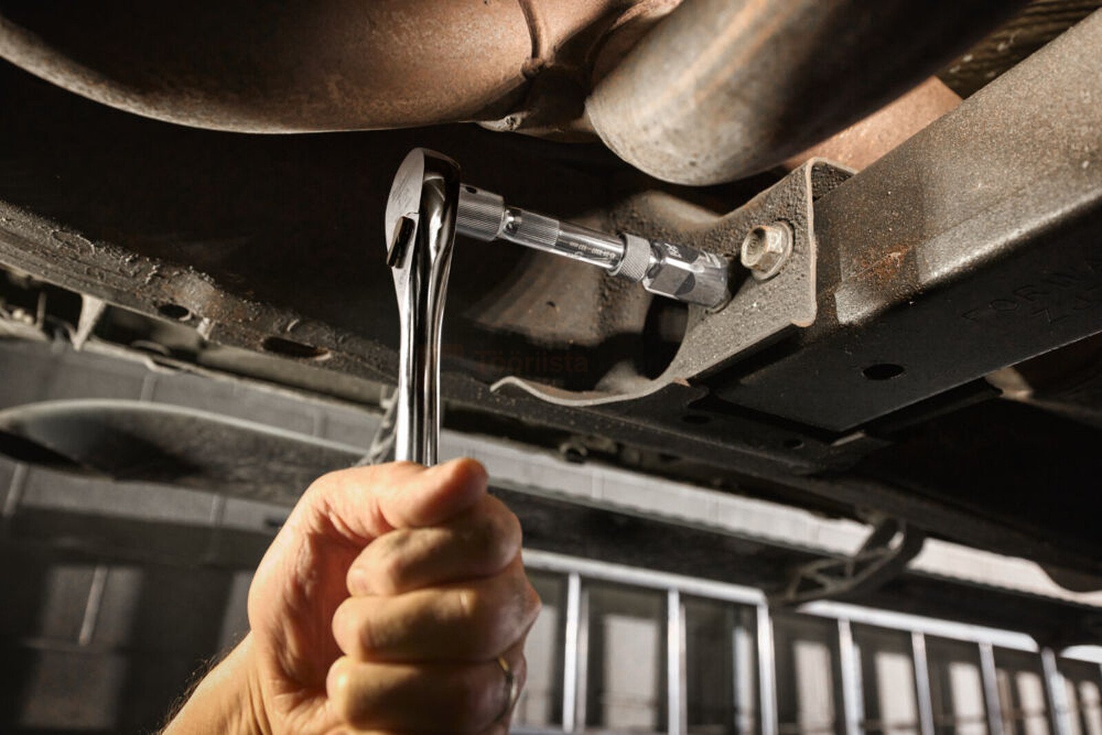 Pildil on näha, kuidas Milwaukee pikenduste komplekti 1/2" abil keeratakse mutrit auto all.