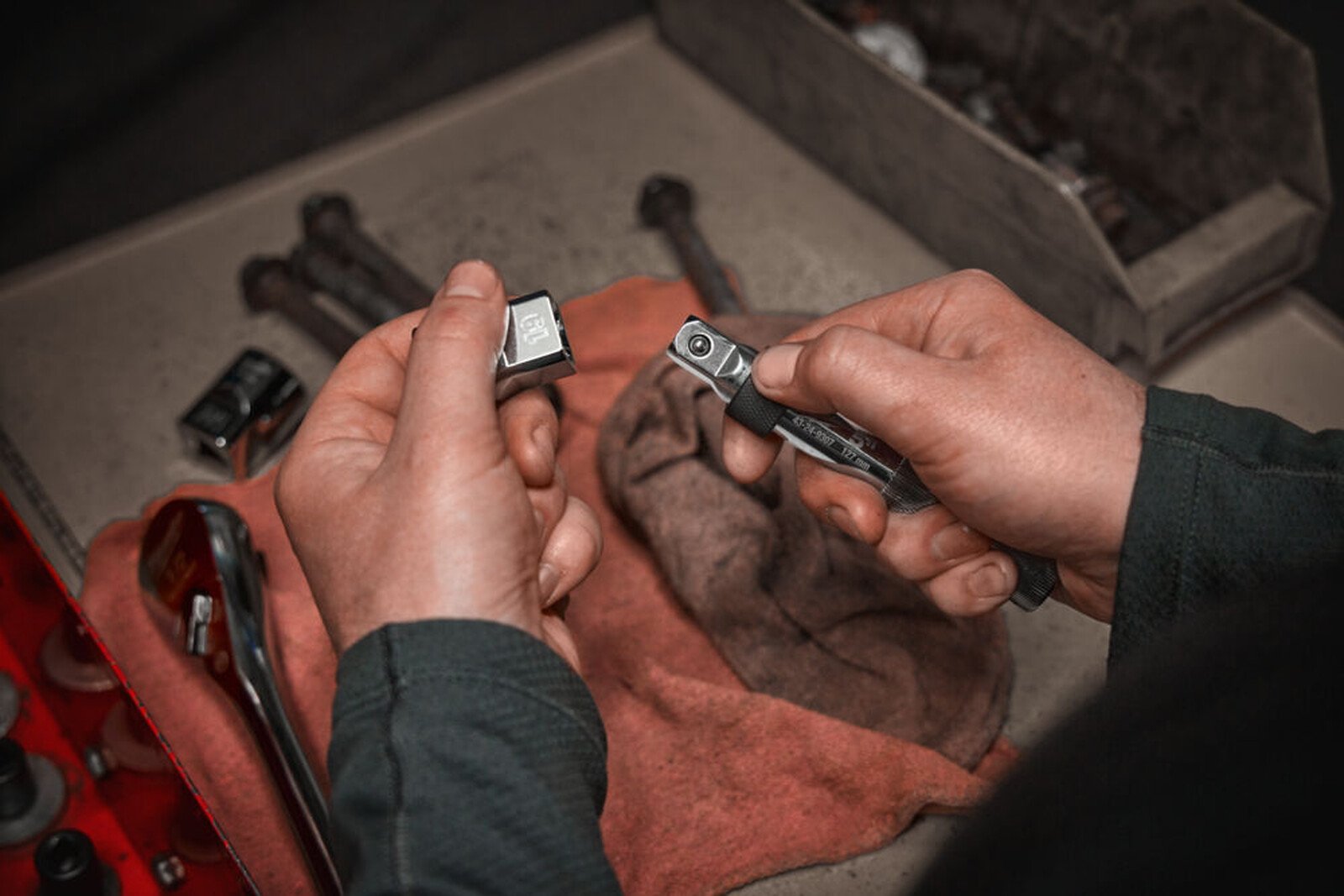 Pildil on mees, kes kasutab Milwaukee 1/2" pikendust, et parandada midagi, ümbritsetuna tööriistadest ja detailidest.