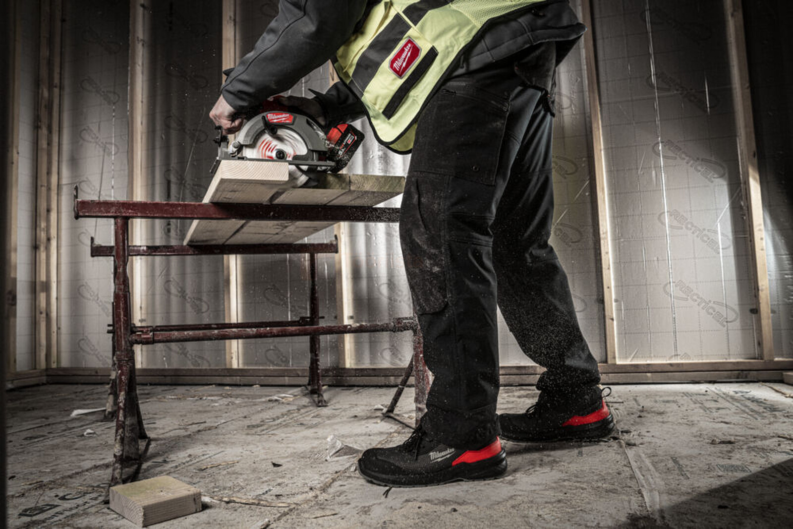 Pildil on ehitustööline, kes kasutab saagi, kandes Milwaukee turvasaapaid Flextred™ S1PS 1M110133 ESD FO SR.