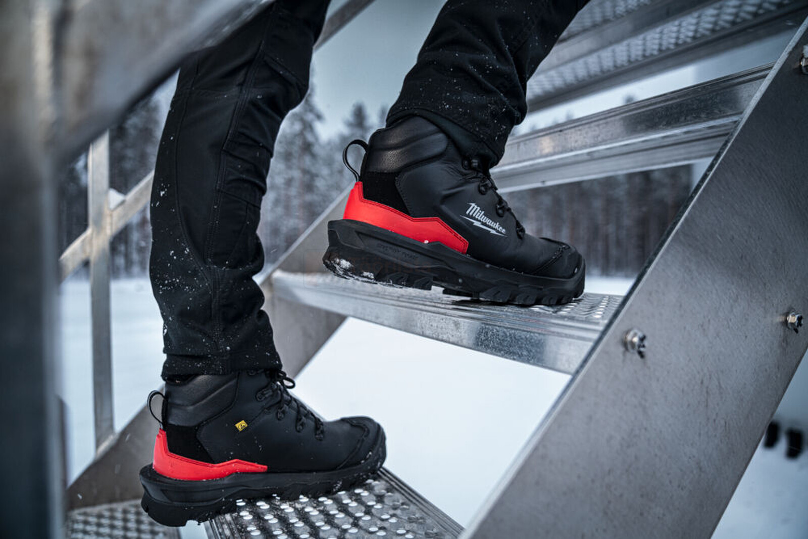 Pildil on näha, kuidas keegi ronib metallist trepist üles, kandes Milwaukee Armourtred™ S3S turvasaapaid.