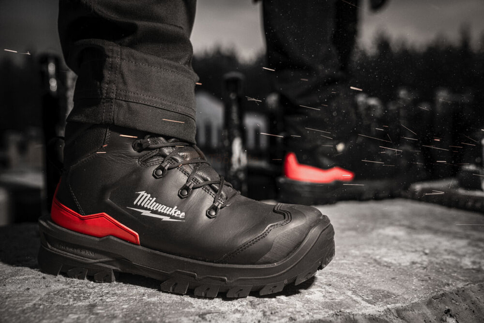 Pildil on näha Milwaukee turvasaapad Armourtred™ S3S, mis on mustad ja punaste detailidega, ning neid kantakse töökeskkonnas.