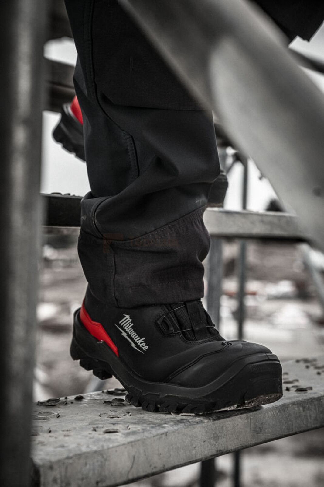 Pildil on näha Milwaukee turvajalatsid Armourtred™ S3S, mis on kantud mustade pükstega mehe poolt, kes kõnnib metallist...