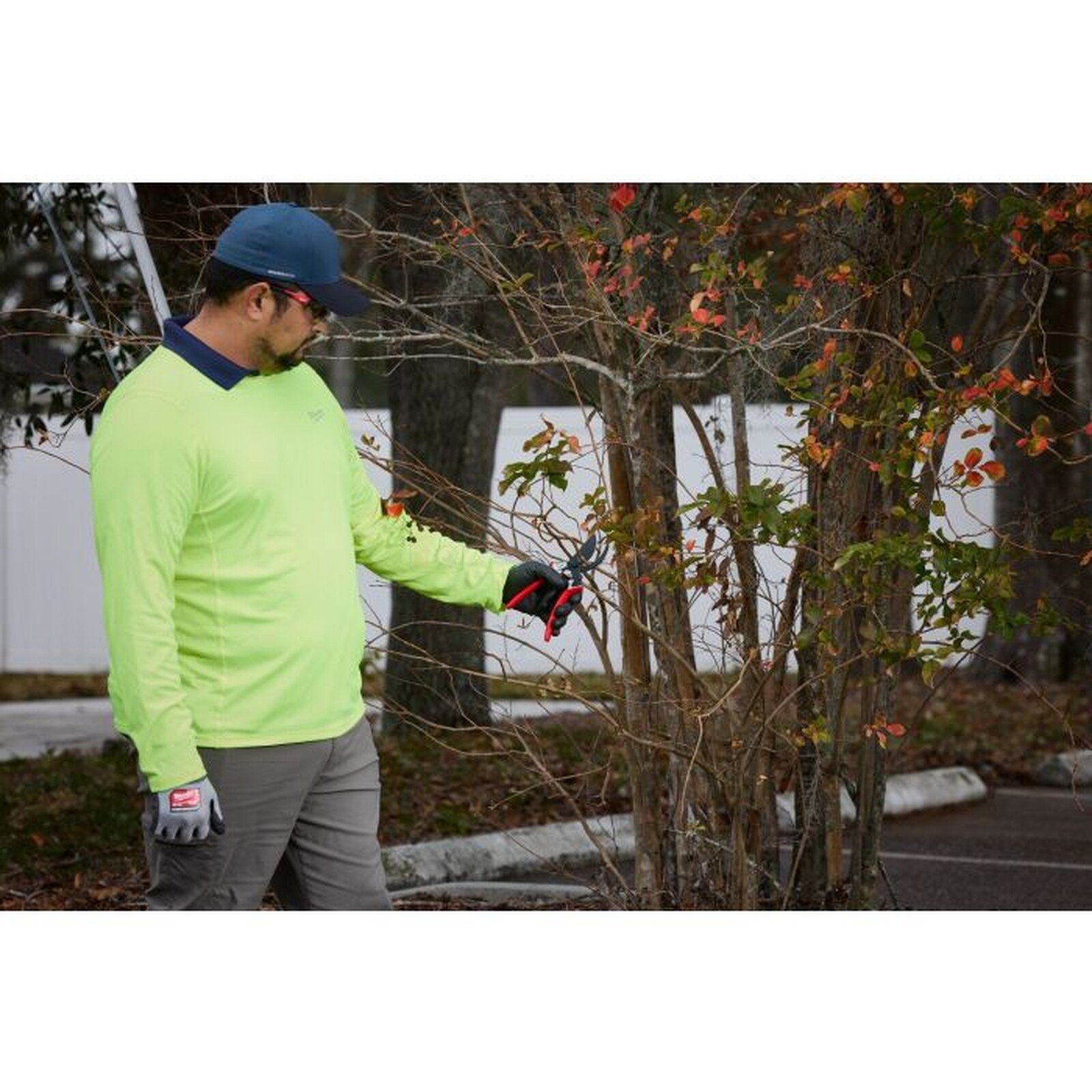 Pildil on mees, kes kasutab Milwaukee oksakääre, et lõigata oksi.
