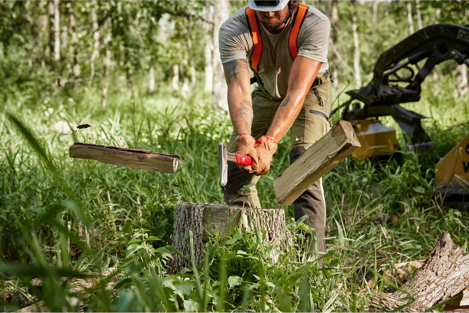 Pildil on metsas töömees, kes kasutab Milwaukee 66 cm kirvest puidu lõhkumiseks.