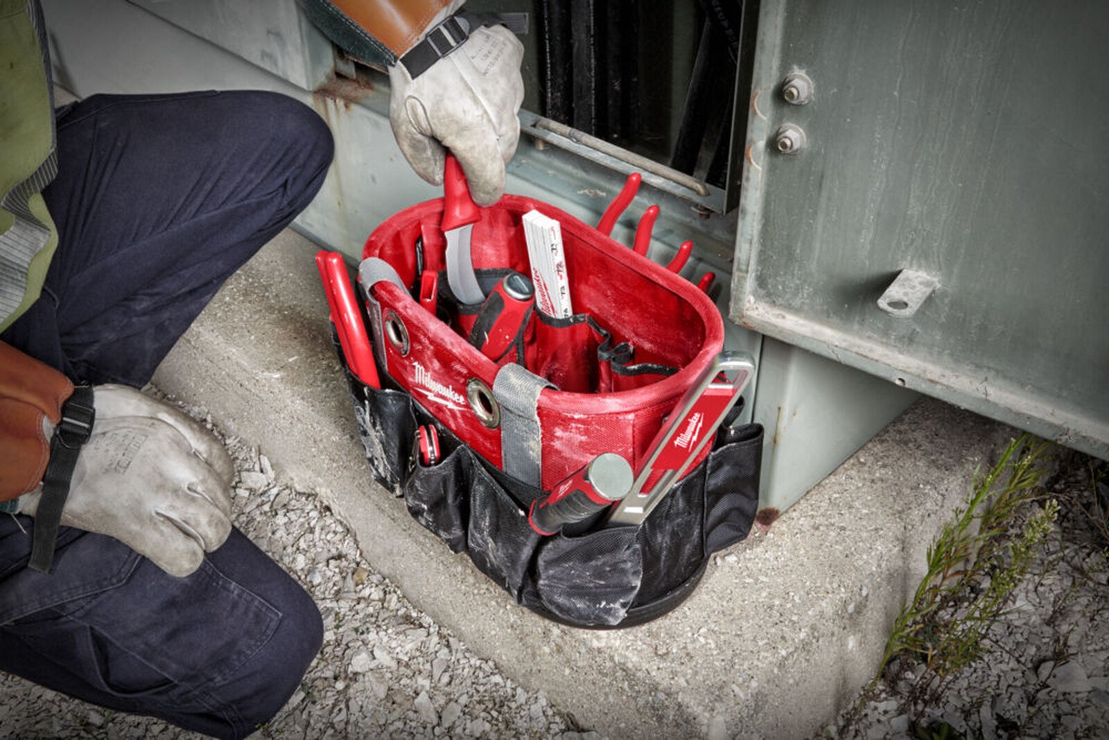 Pildil on Milwaukee ovaalne kandekott tööriistadele, mida kasutab töömees, kes töötab metallist ukse juures.