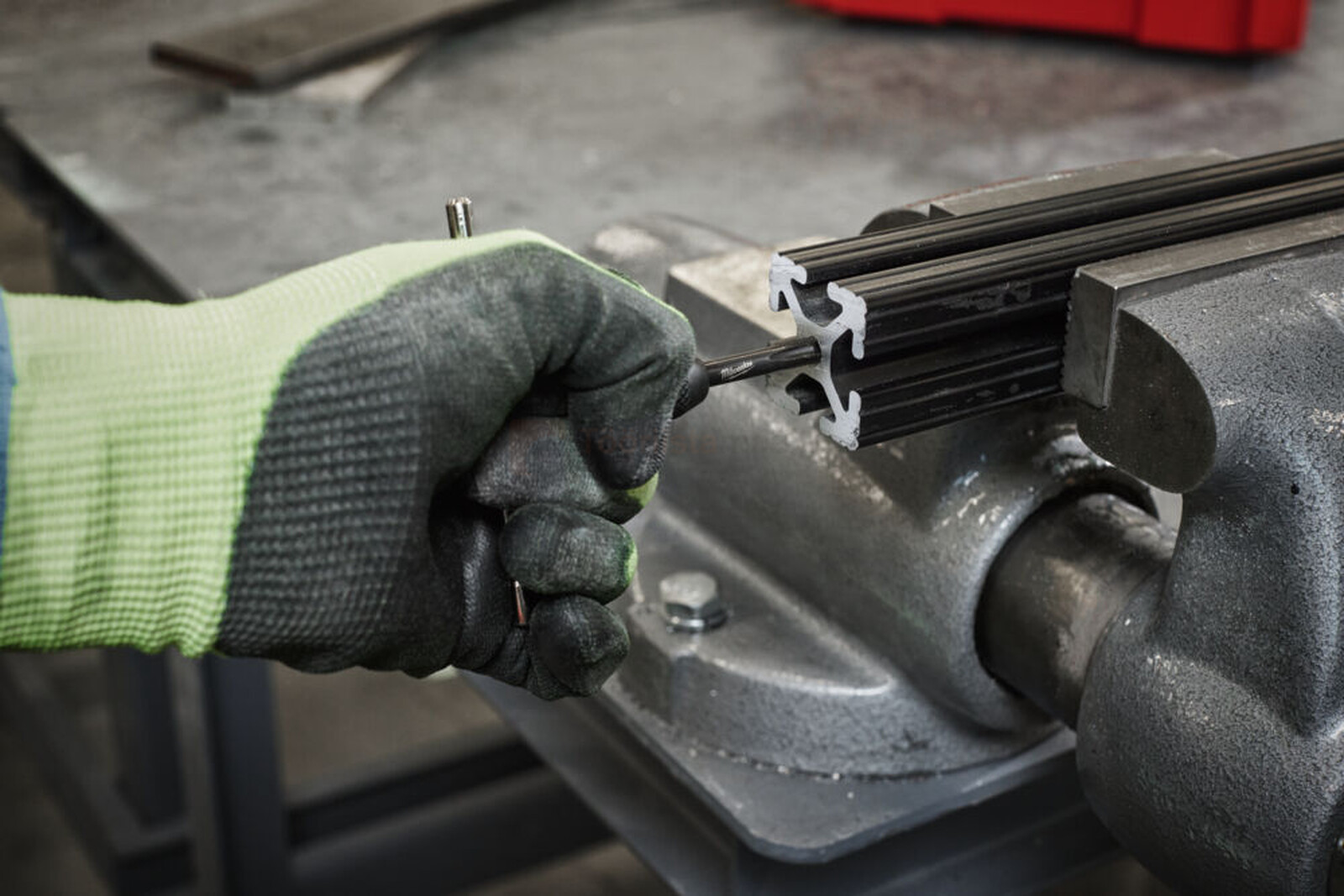 Pildil on Milwaukee keermestajate komplektiga töötav inimene, kes kasutab tööriista metallist detaili keermestamiseks.