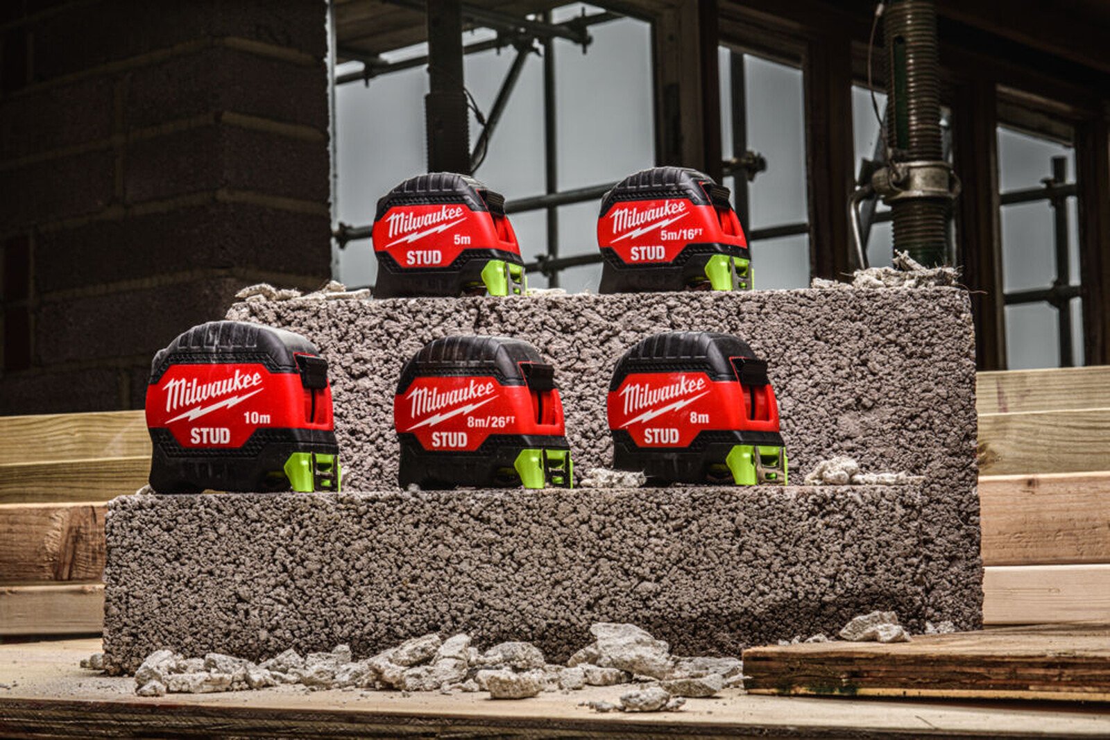Pildil on näha mitu Milwaukee STUD™ III mõõdulinti, mis on paigutatud betoonplokile ehitusplatsi taustal.