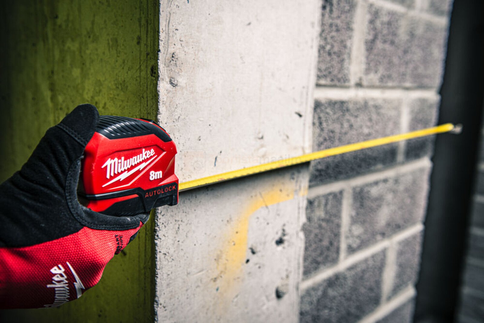 Pildil on Milwaukee mõõdulint Autolock 8 m x 25 mm, mida kasutatakse mõõtmiseks betoonseina vastu.