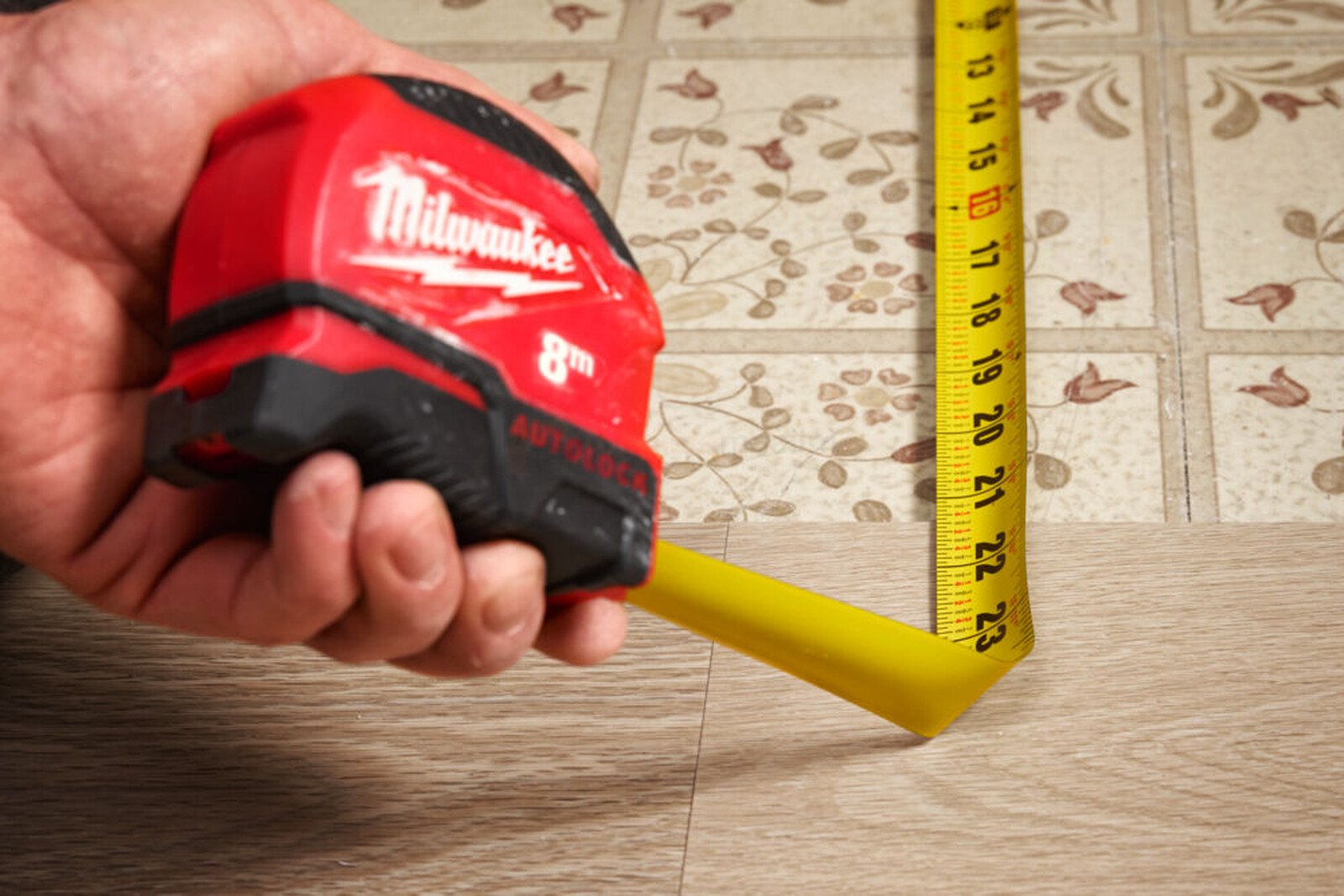 Pildil on käes Milwaukee Autolock 8 m x 25 mm mõõdulint, millega mõõdetakse põrandat.