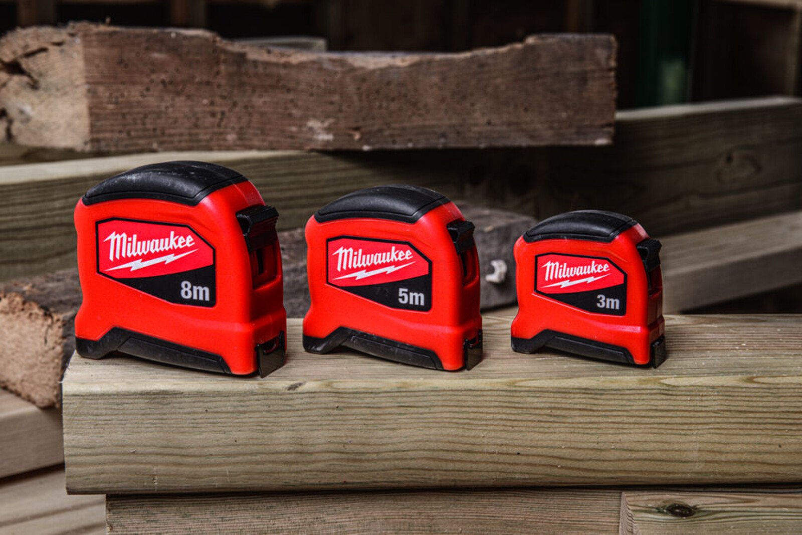 Pildil on kolm erineva suurusega Milwaukee kompaktset mõõdulinti, mis on asetatud puidust pinnale.