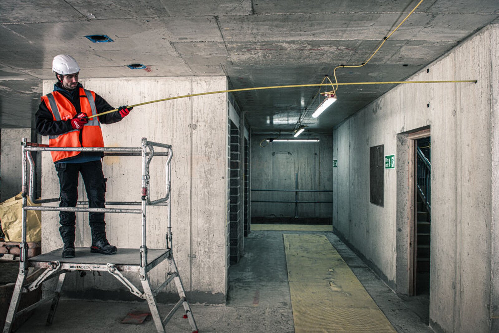 Pildil on ehitustöölise Milwaukee mõõdulindiga 8 m x 35 mm mõõtmas ruumi kõrgust, seistes tellingutel betoonist...