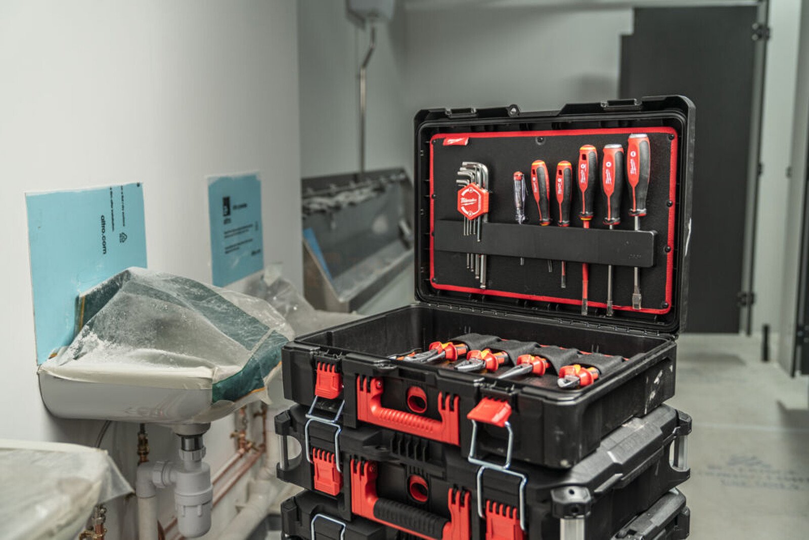 Pildil on avatud Milwaukee PACKOUT™ 74-osaline tööriistakomplekt, mis on virnastatud teiste kastide peale ja sisaldab...