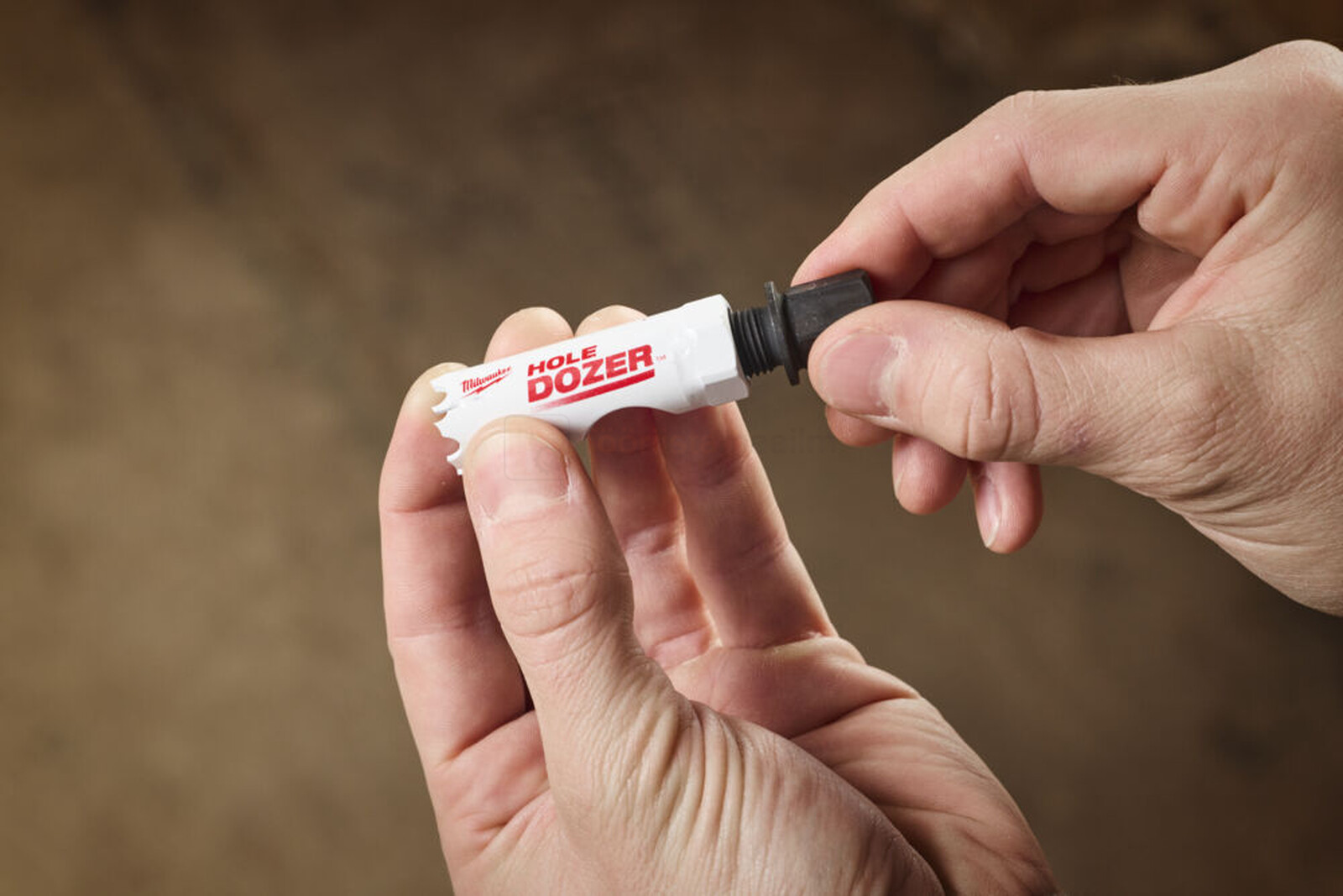 Pildil on näha, kuidas inimene hoiab käes Milwaukee augusae adapterit QUIK-LOK S, mis on mõeldud augusaagidele.