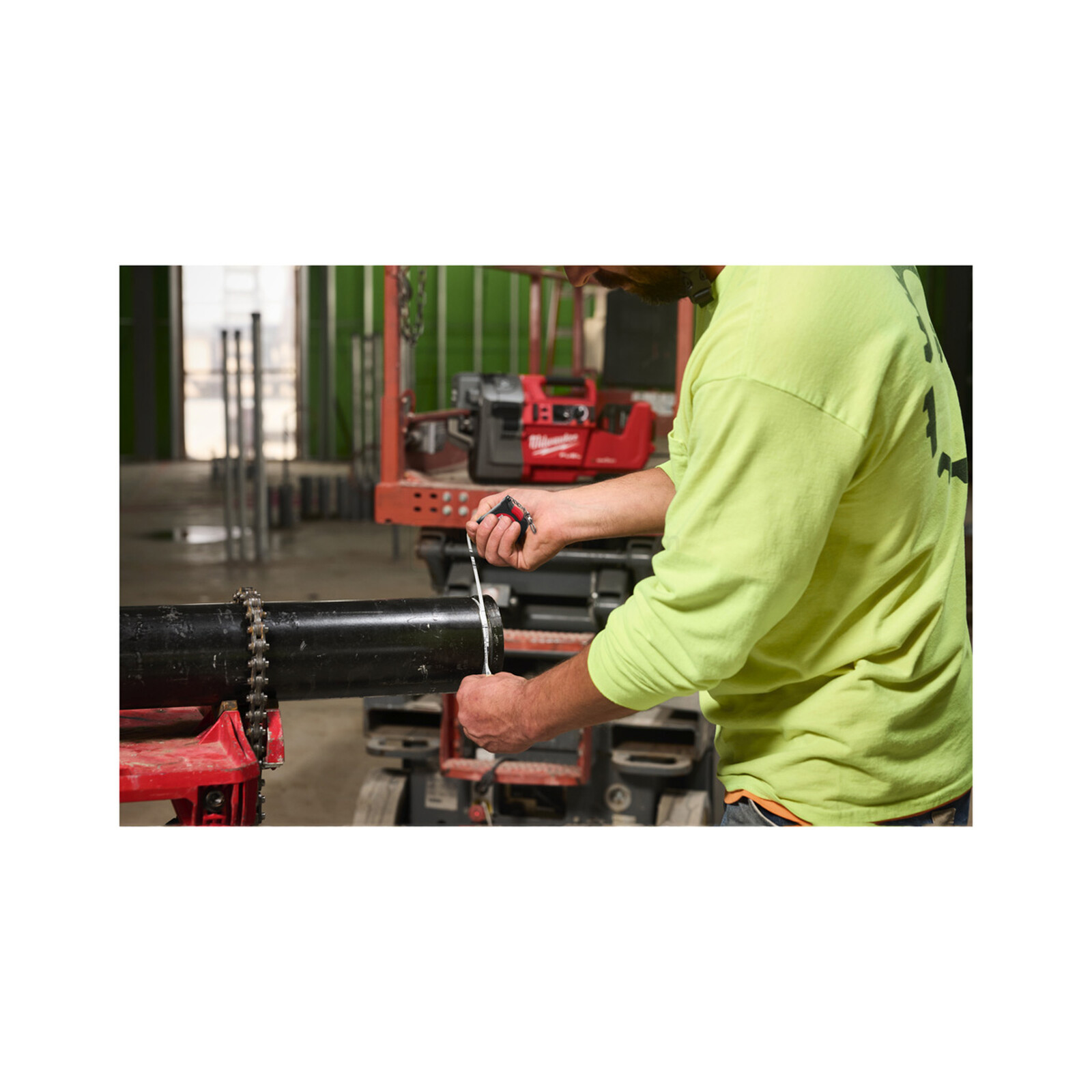 Pildil on ehitustöötaja, kes kasutab Milwaukee mõõdulinti torudele, et mõõta musta toru pikkust.