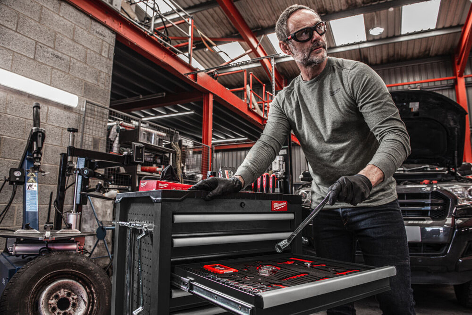 Pildil on mees, kes kasutab Milwaukee tööriistakäru, millel on 7 sahtlit, halli värvi ja mis on töökojas.