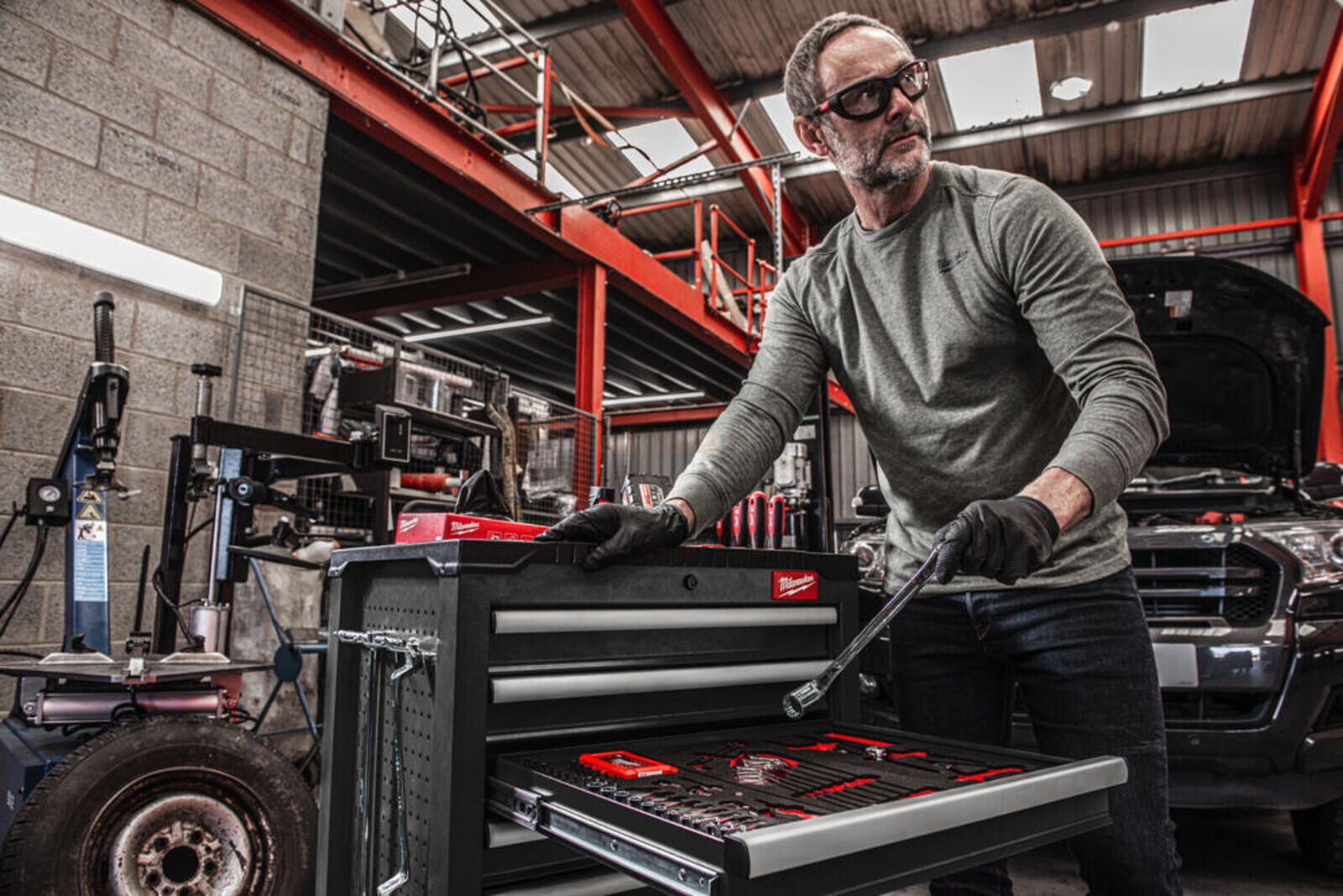 Pildil on mees, kes kasutab Milwaukee tööriistakomplekti halli tööriistakäruga, mille sahtel on avatud ja nähtavad on...
